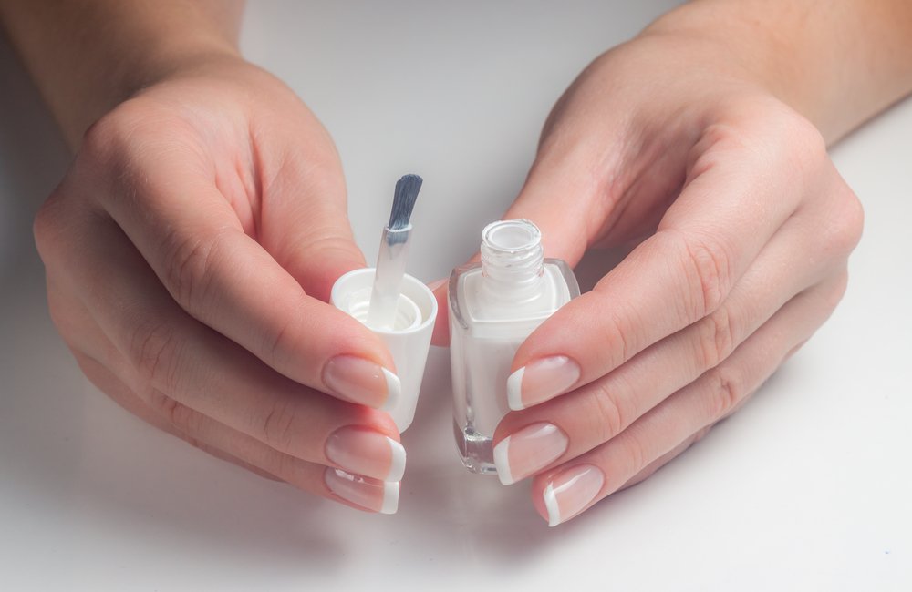 Manos con manicura franesa sosteniendo una botella de esmalte de uñas blanco. | Foto: Shutterstock