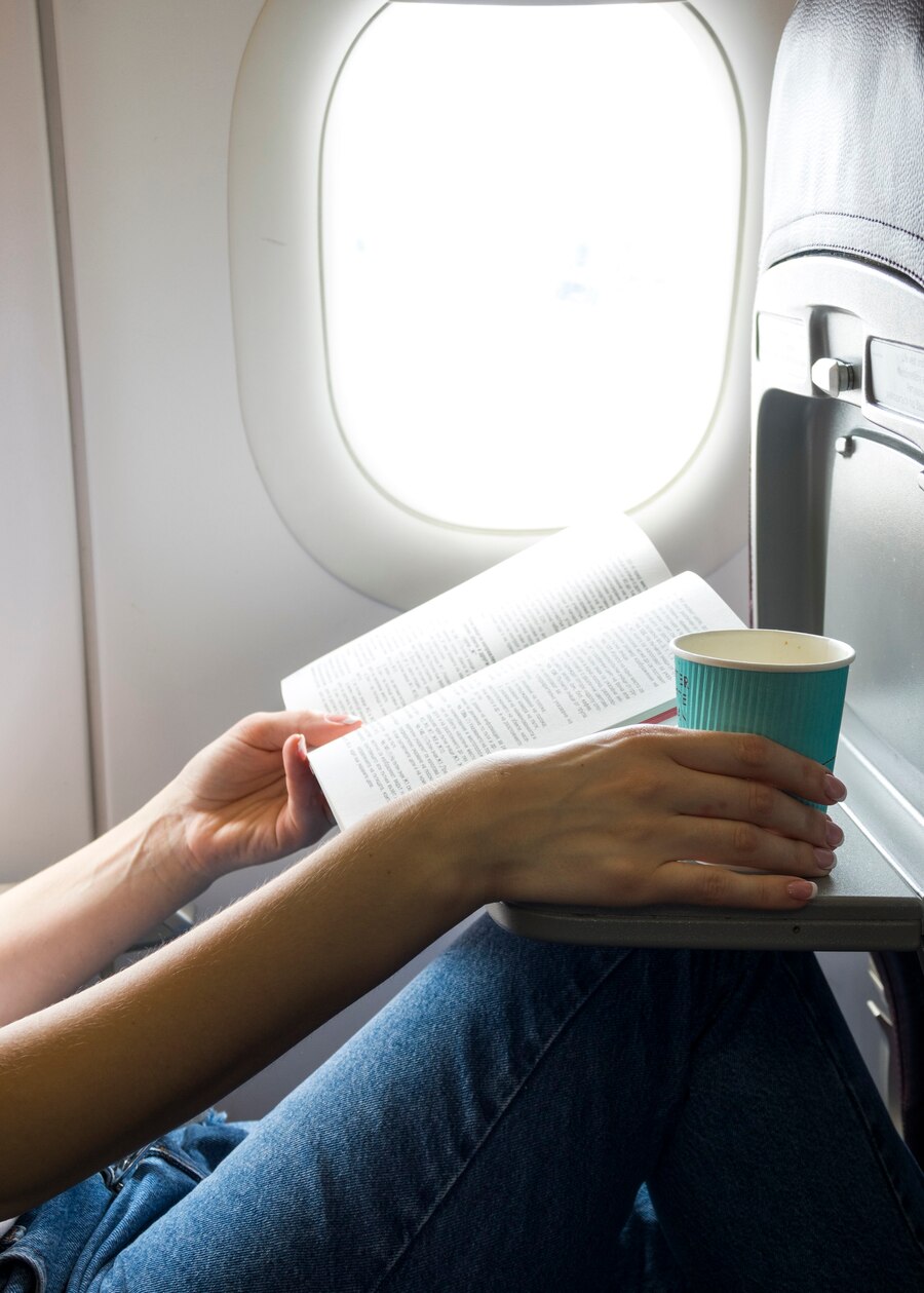 Una mujer con un libro y un café en el asiento de una ventana | Fuente: Freepik