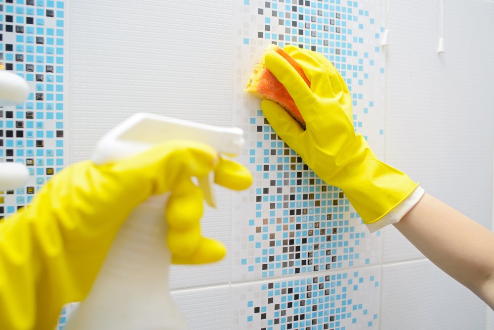 Manos con guantes limpiando la superficie de baldosas en el baño. | Foto: Shutterstock