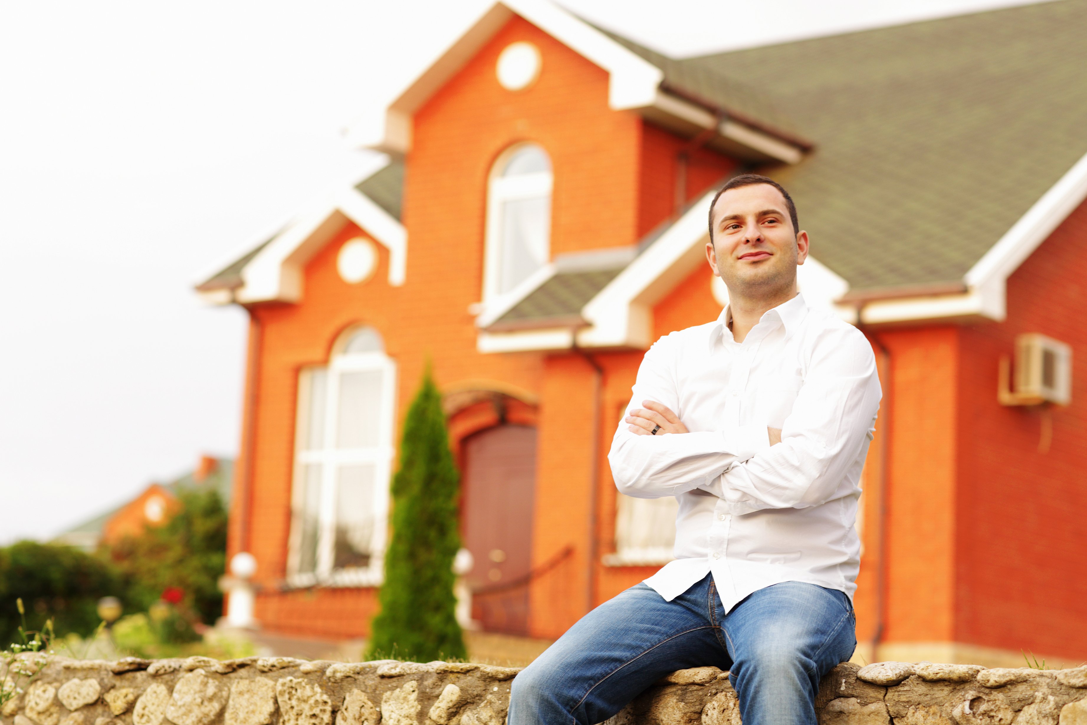 Hombre feliz sentado frente a una casa de ladrillos anaranjados. | Foto: Shutterstock