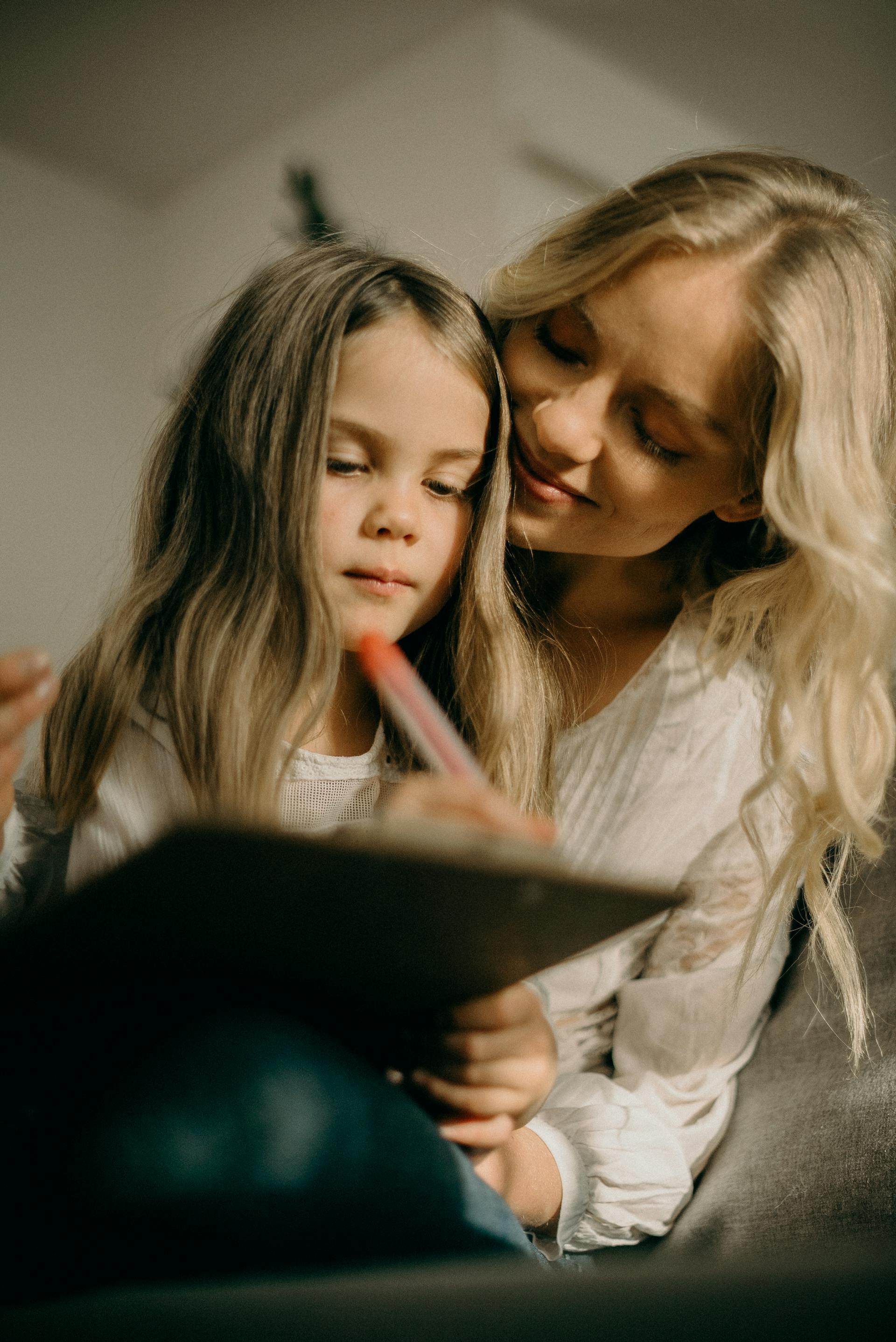 Una niña dibujando algo en un papel mientras está sentada junto a una mujer rubia | Fuente: Pexels