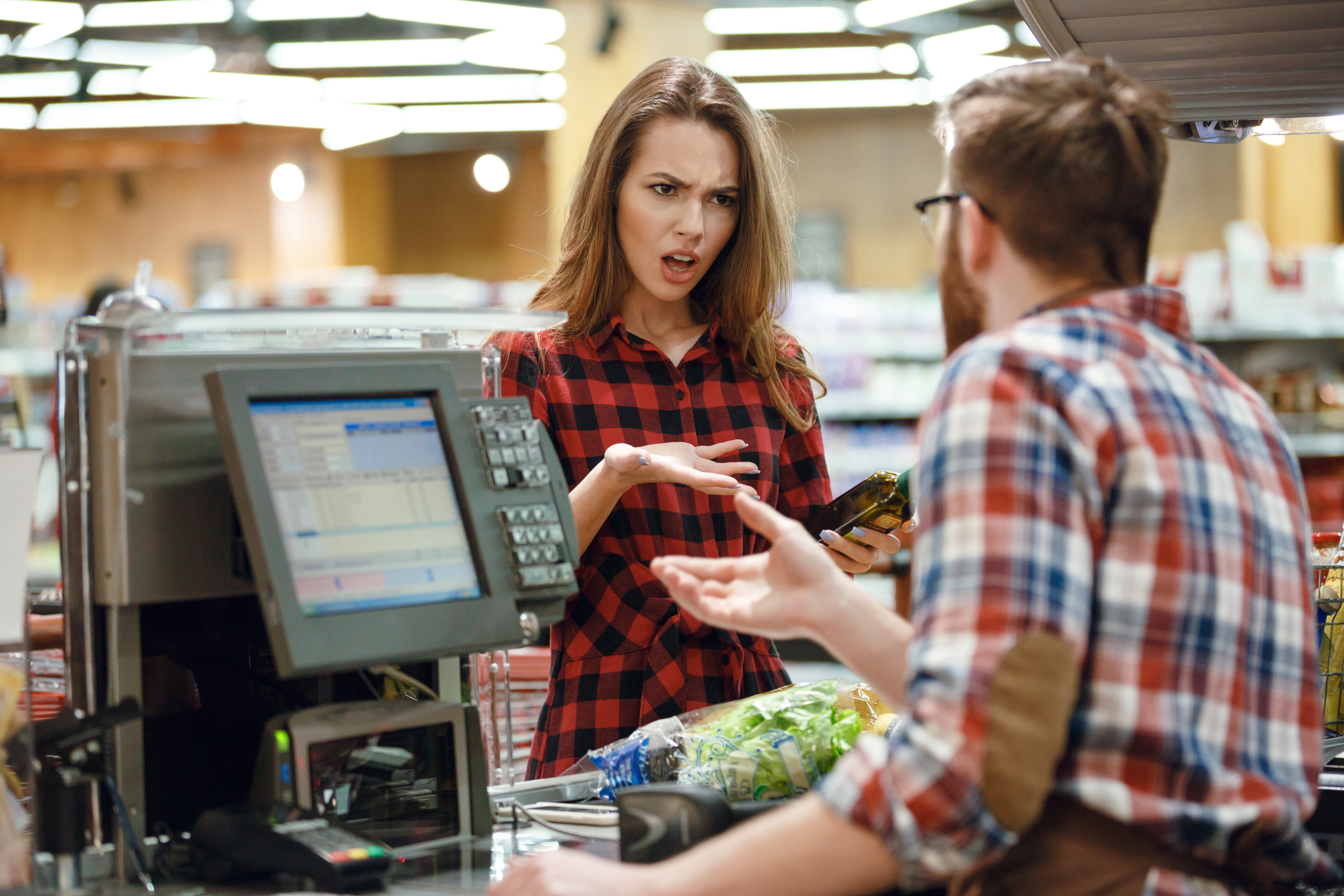 Una cajera enfadada atendiendo a un cliente masculino | Fuente: Shutterstock