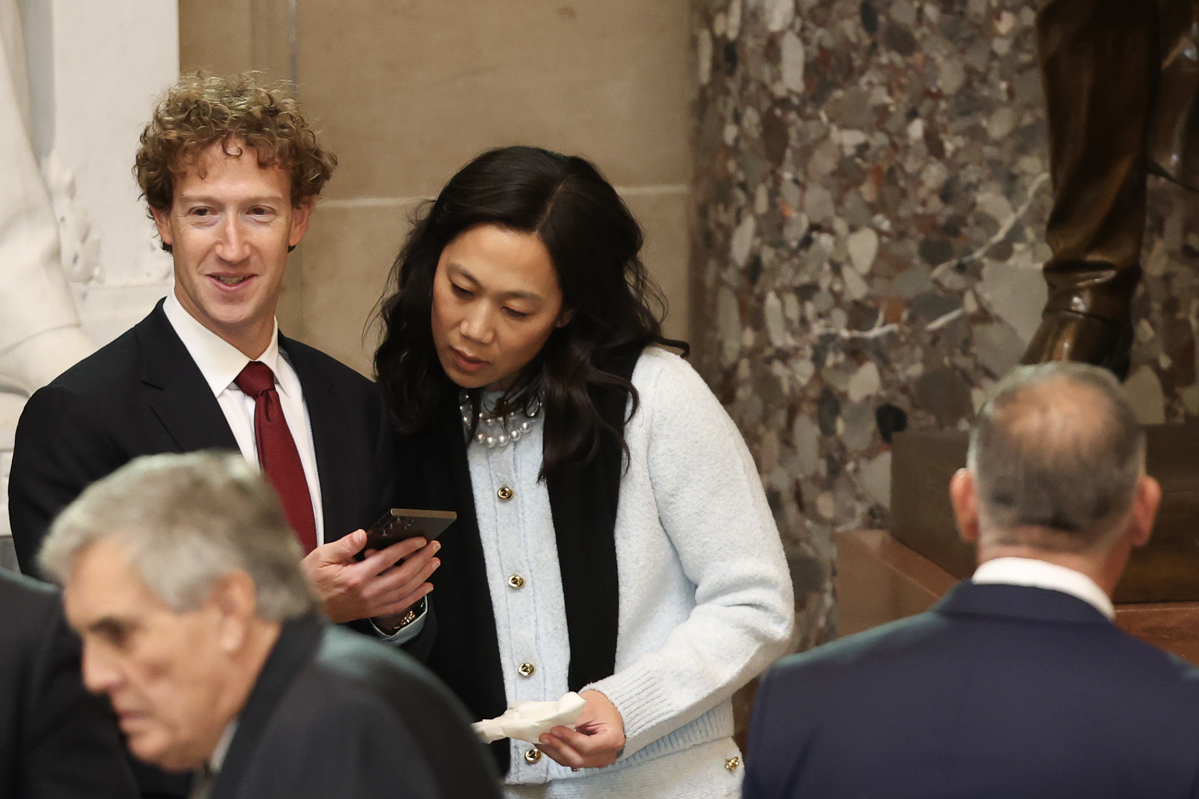 Priscilla Chan mirando el teléfono de Mark Zuckerberg mientras están uno al lado del otro durante la toma de posesión de Donald Trump. | Fuente: Getty Images