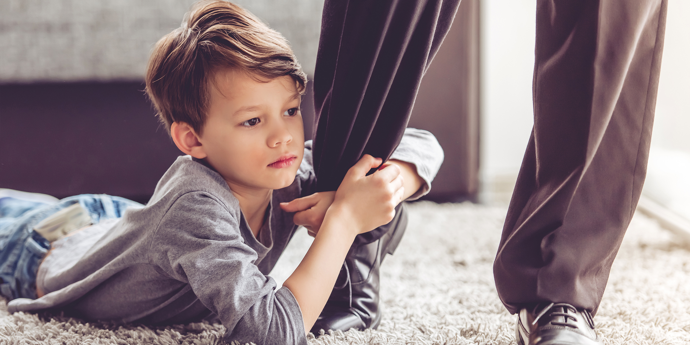 Un niño agarrado a la pierna de un adulto | Fuente: Shutterstock