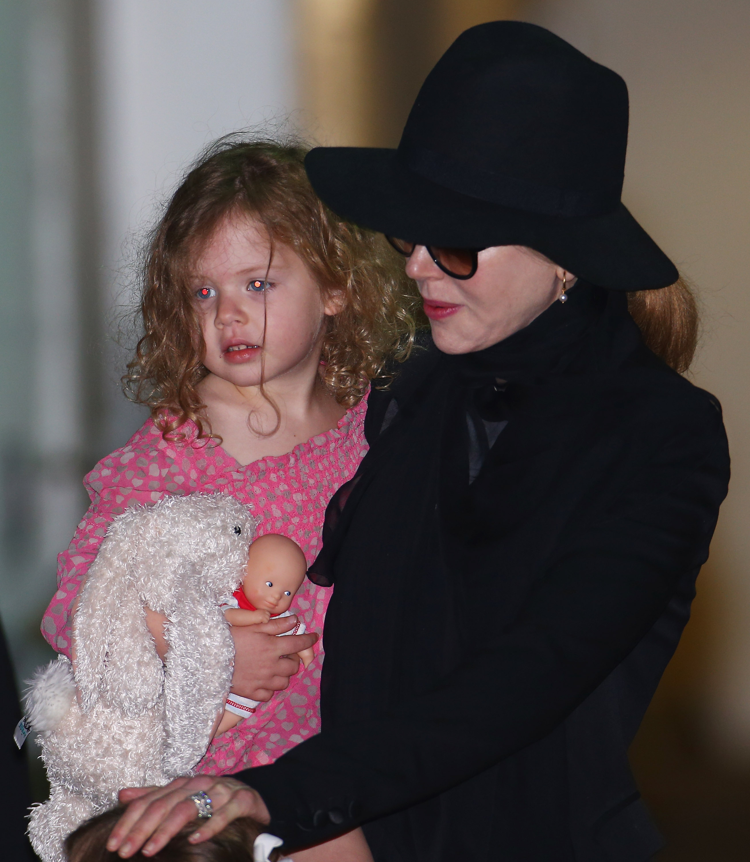 Nicole Kidman lleva en brazos a su hija Faith Margaret, de tres años, durante un viaje en familia en enero de 2014. Faith sujeta con fuerza un conejito de peluche y una muñequita, mientras su madre la mantiene bien cerca. | Fuente: Getty Images
