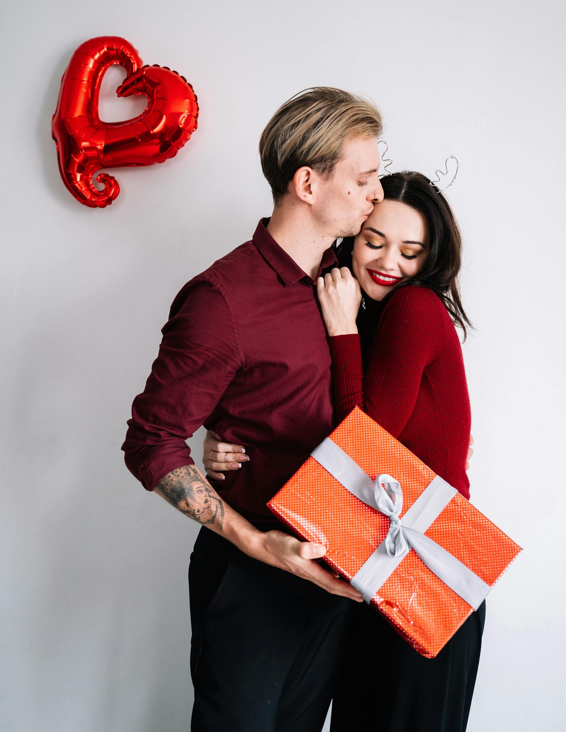 Un hombre besa a una mujer mientras sostiene una caja de regalo | Foto: Pexels
