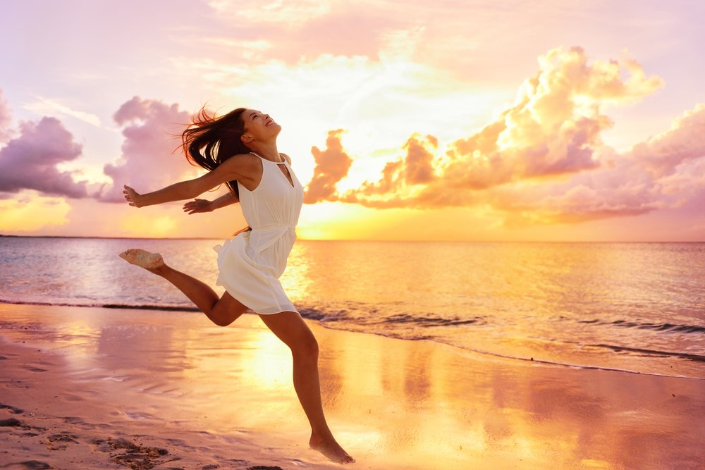 Mujer asiática feliz saltando de alegría en la playa en una puesta del sol. | Fuente: Shutterstock