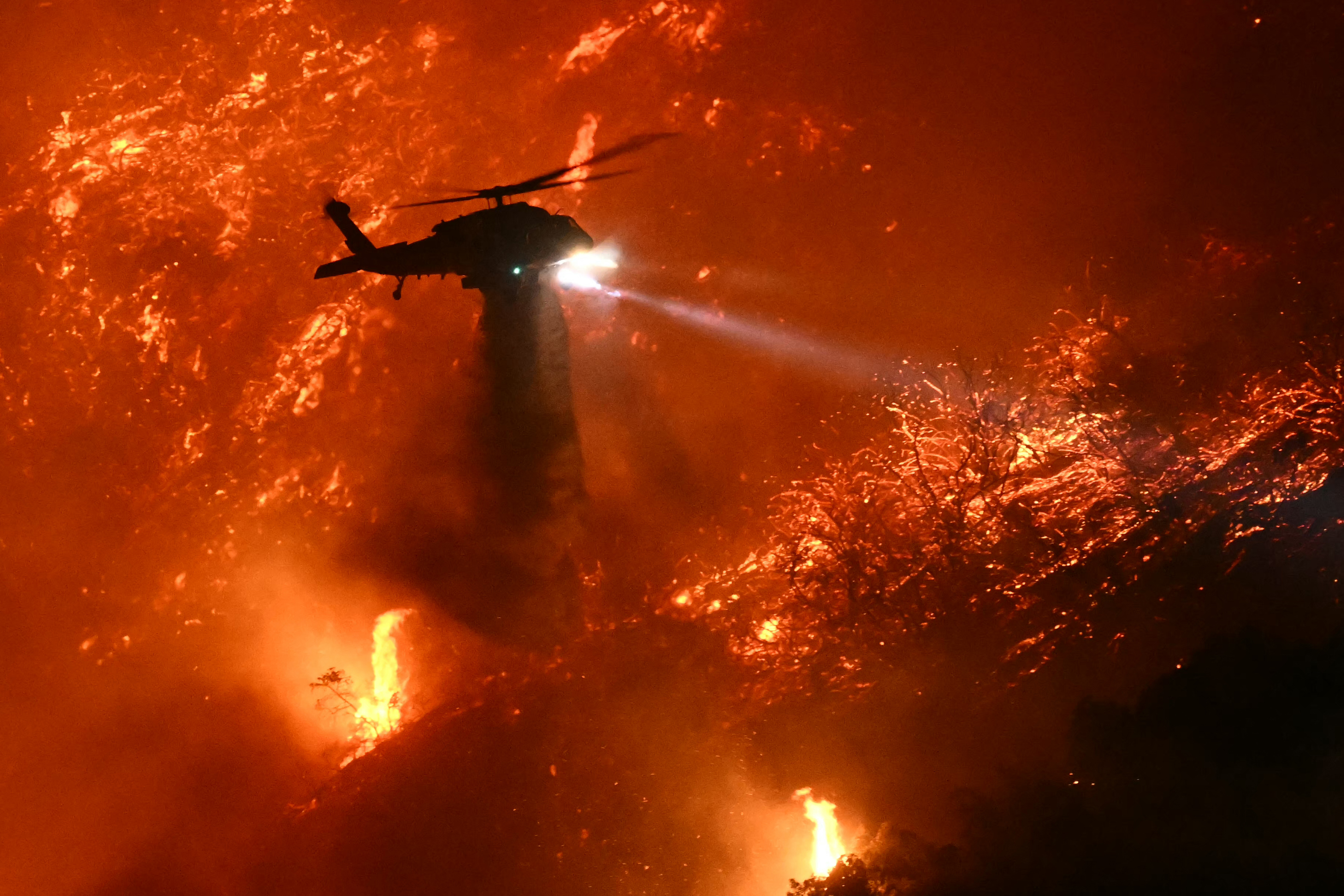 Un helicóptero de extinción de incendios deja caer agua mientras el incendio de Palisades crece cerca del barrio de Mandeville Canyon y Encino, California, el 11 de enero de 2025 | Fuente: Getty Images