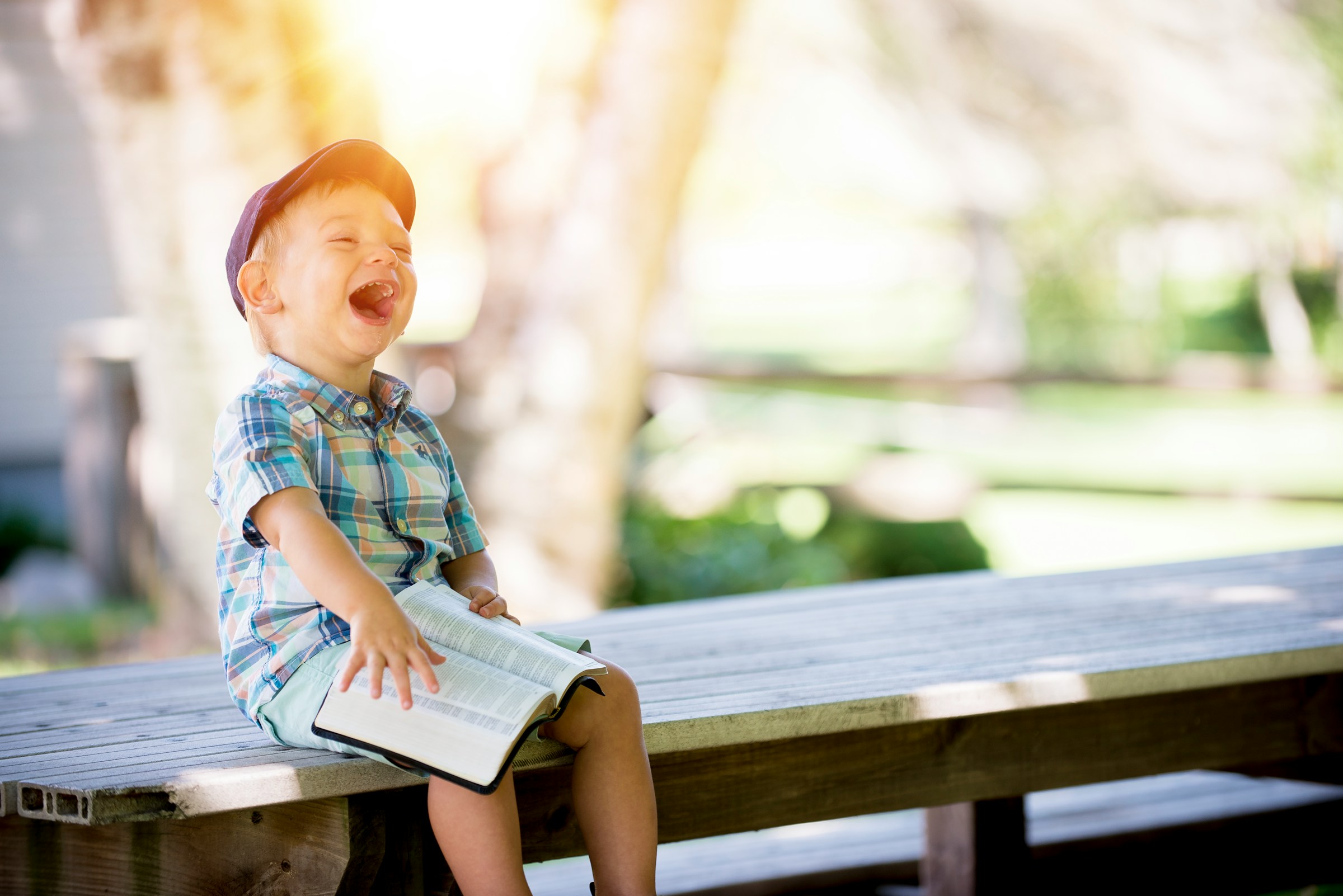 Un niño se ríe sentado en un banco y con un libro en la mano | Fuente: Unsplash