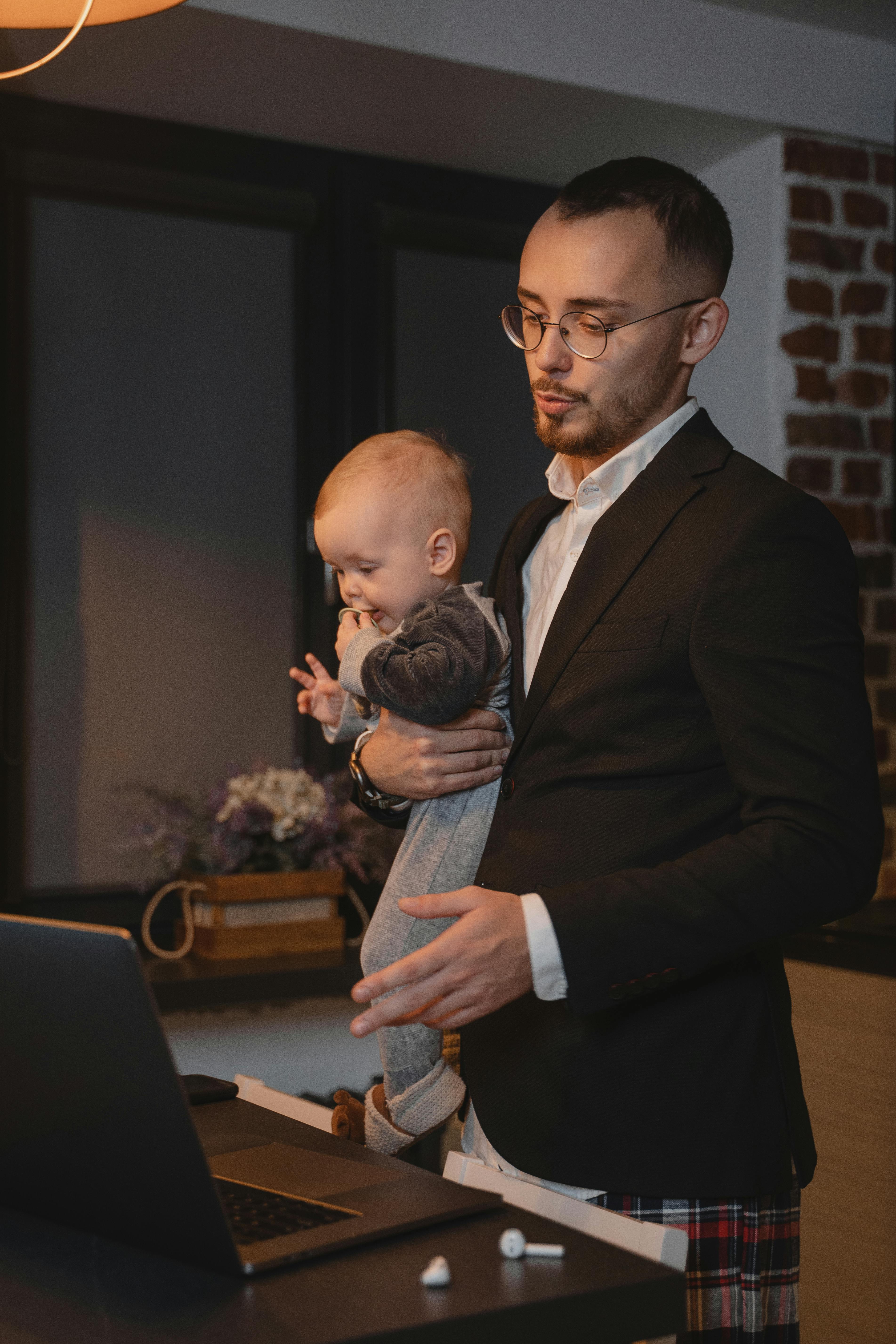 Un padre con un bebé en brazos mientras habla con su portátil | Foto: Pexels