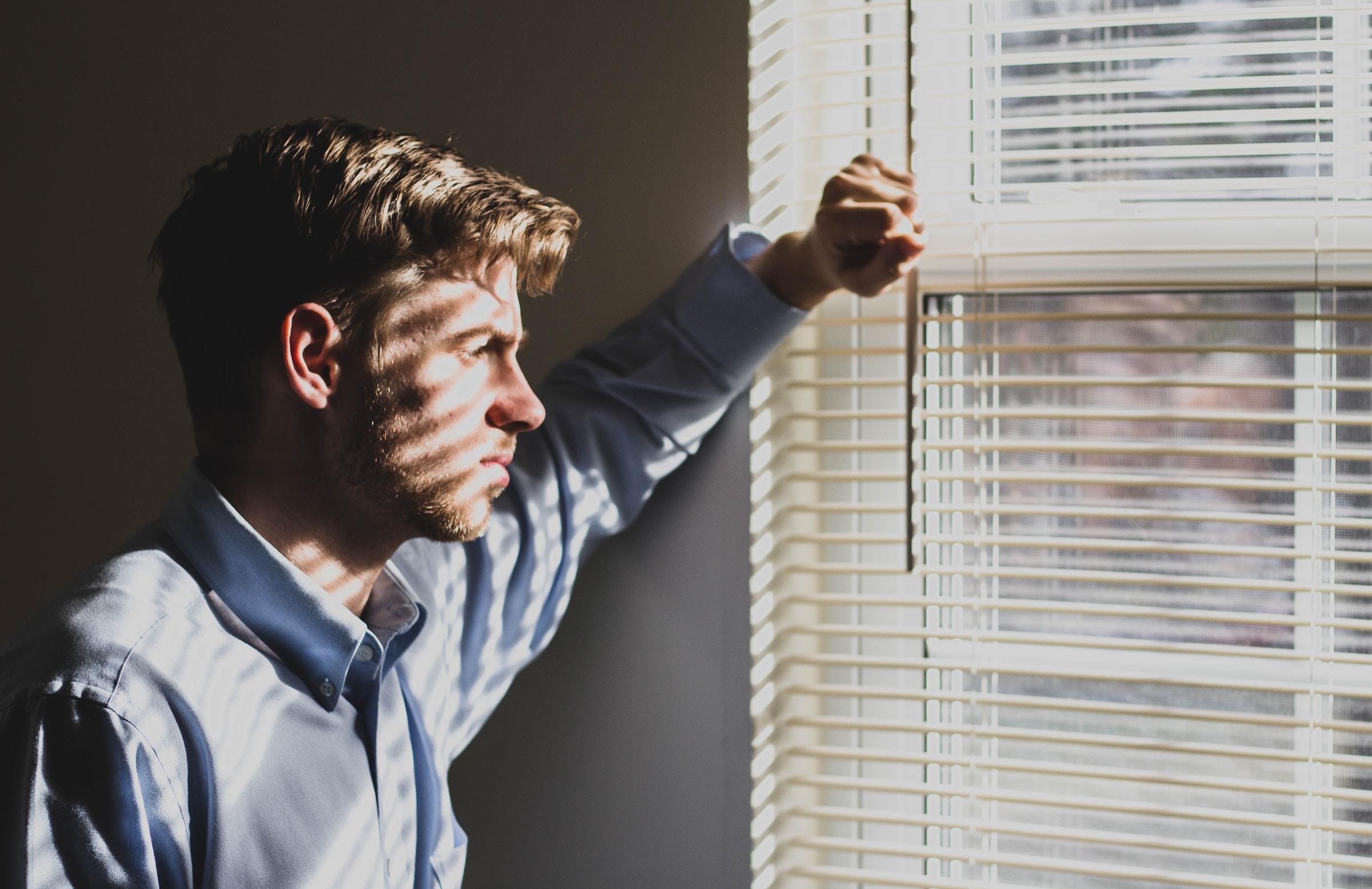 Un hombre mirando al exterior a través de las persianas de la ventana | Fuente: Unsplash