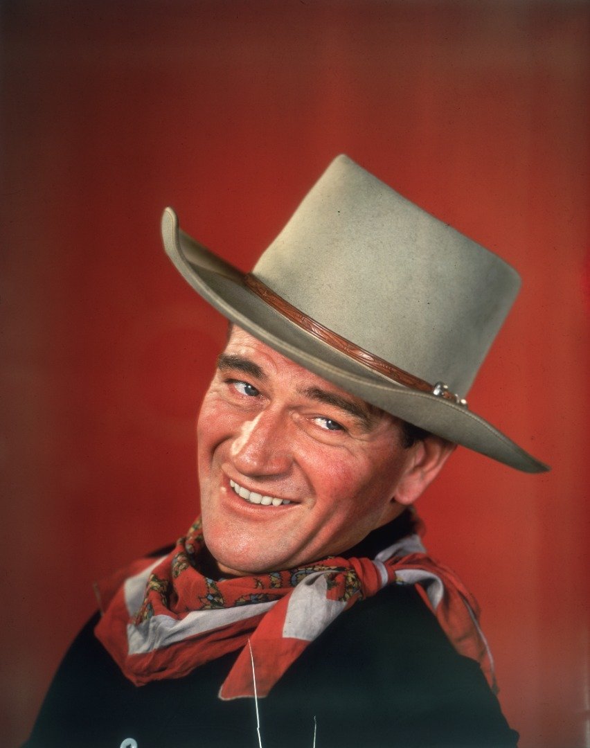 John Wayne sonriendo ante un fondo rojo, vestido con indumentaria del Oeste | Foto: Getty Images