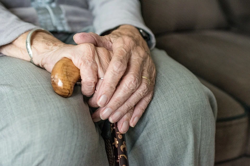 Anciana sosteniendo un bastón mientras está sentada en un sofá. | Foto: Pixabay