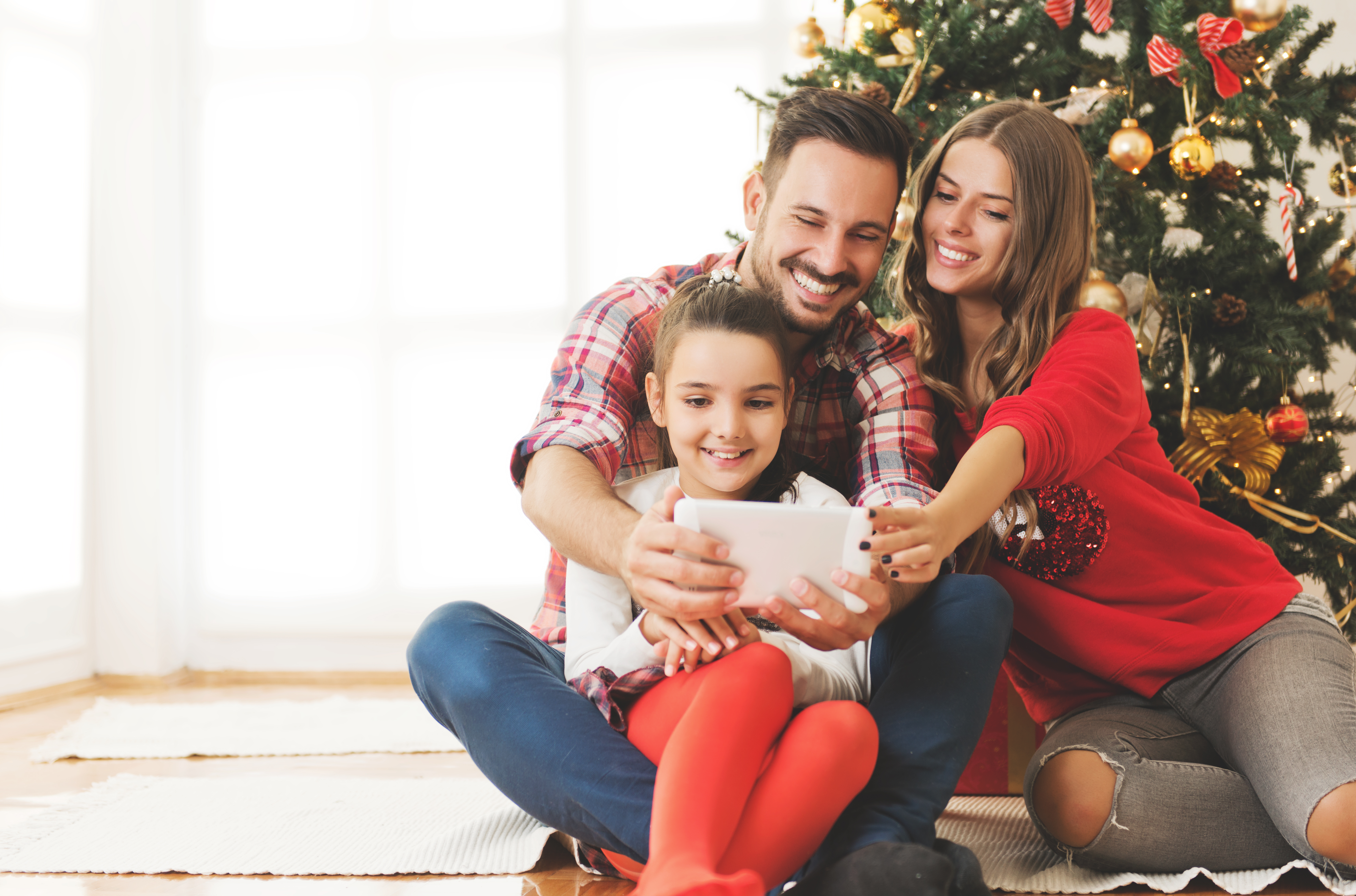 Una niña jugando con un iPad con su padre y su madre con un árbol de Navidad de fondo. | Foto: Shutterstock