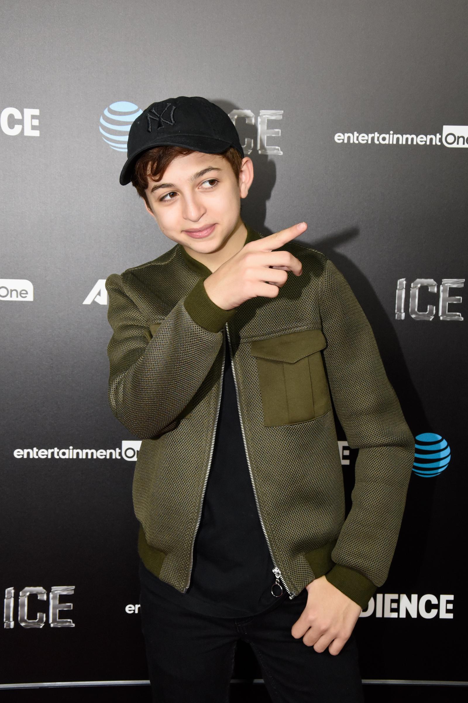 J.J. Totah llega al estreno de "Ice", de Audience Network, en los cines ArcLight de Hollywood, California, con una chaqueta texturizada de color verde oliva, una gorra de béisbol negra y unos pantalones oscuros. Totah señala hacia un lado mientras posa para los fotógrafos. | Fuente: Getty Images