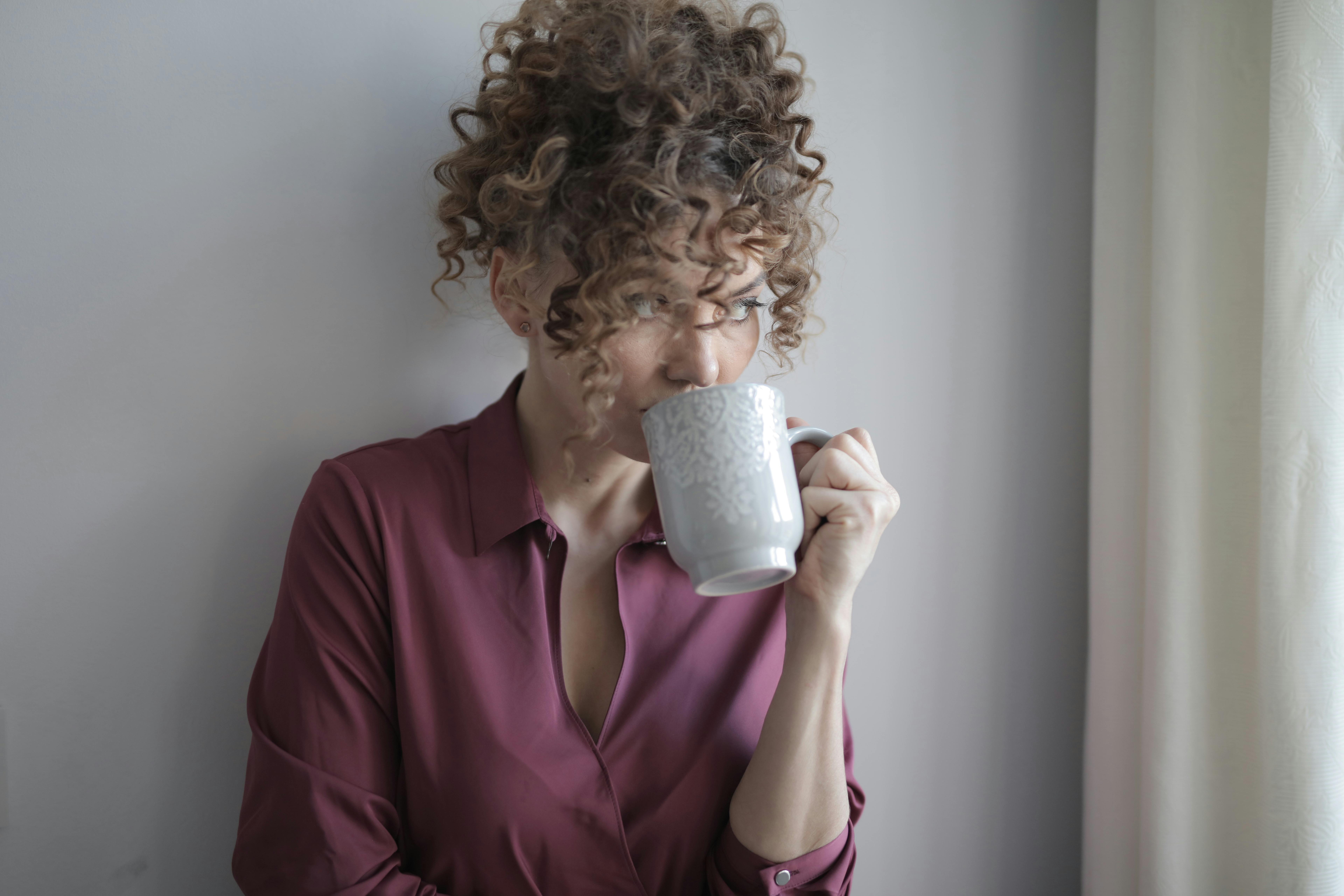 Una mujer sorbe de una taza, mirando pensativamente por una ventana | Fuente: Pexels