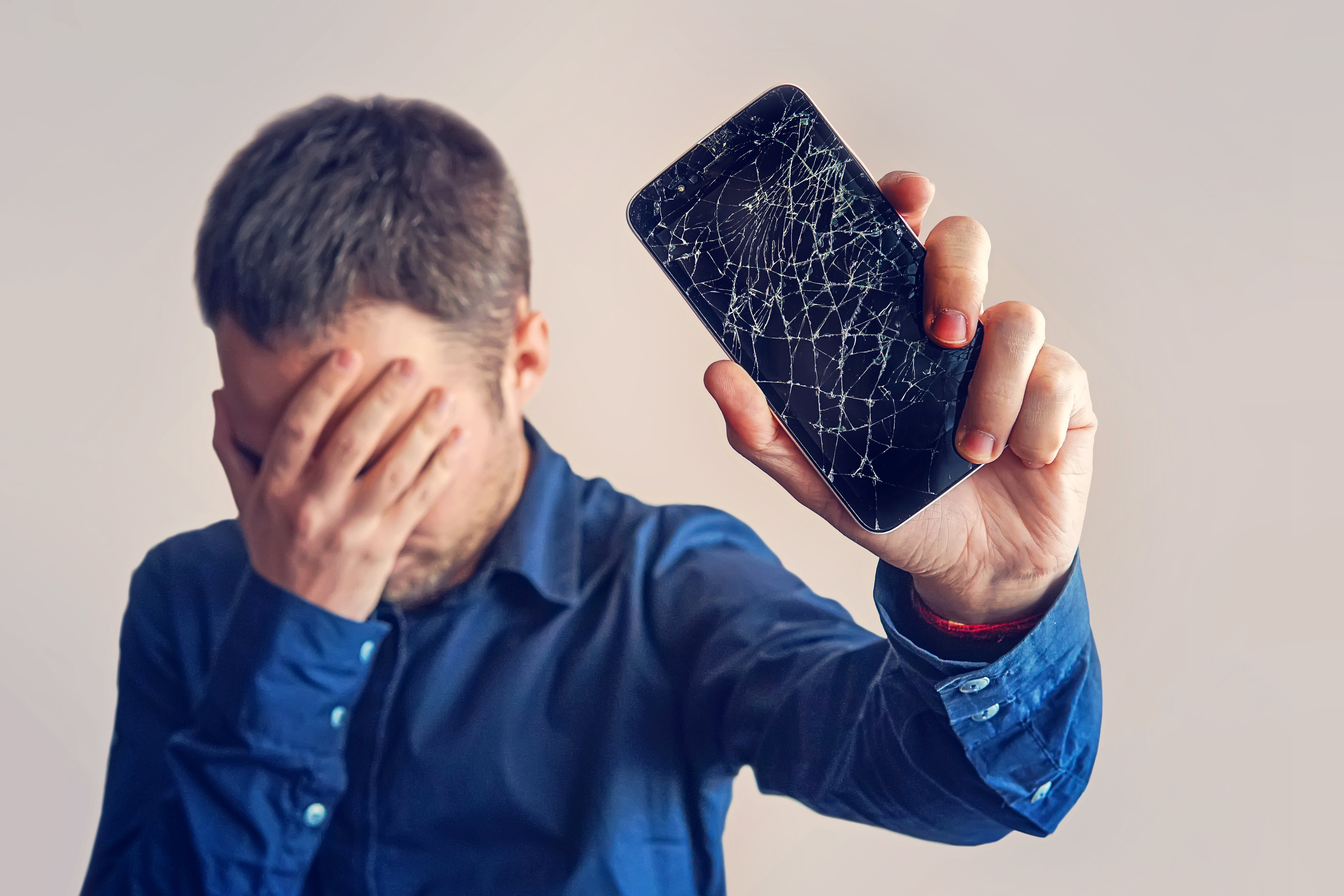 Un tipo sujetando un teléfono con la pantalla rota | Fuente: Shutterstock