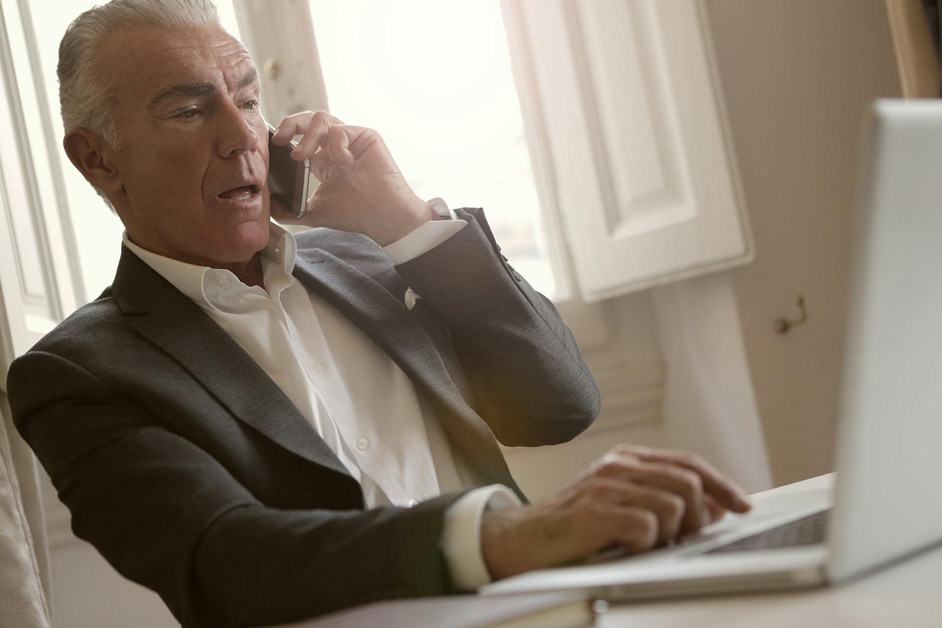 Un hombre preocupado hablando por teléfono mientras usa su portátil | Fuente: Pexels