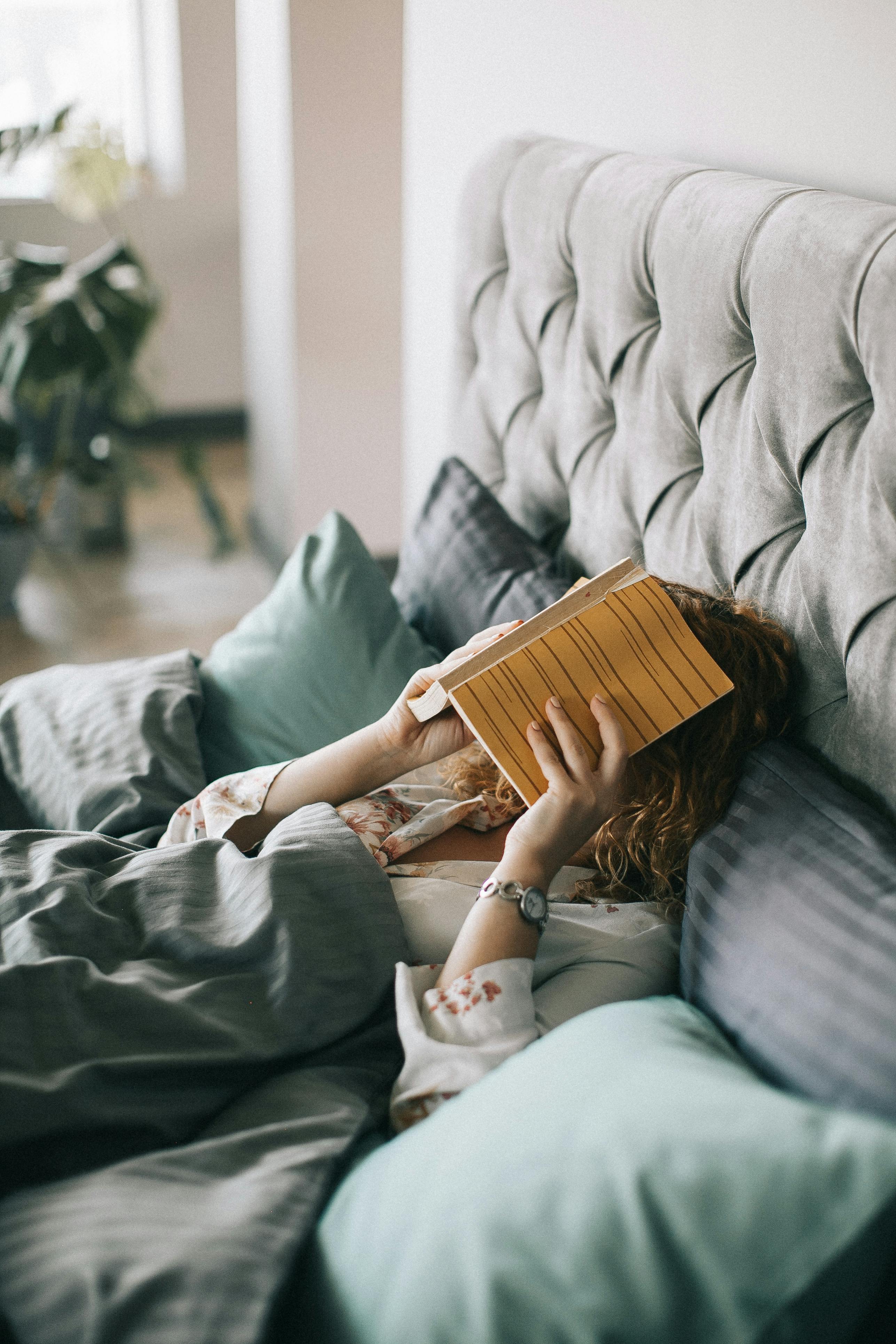 Una mujer tumbada en la cama con un libro cubriéndole la cara | Fuente: Pexels