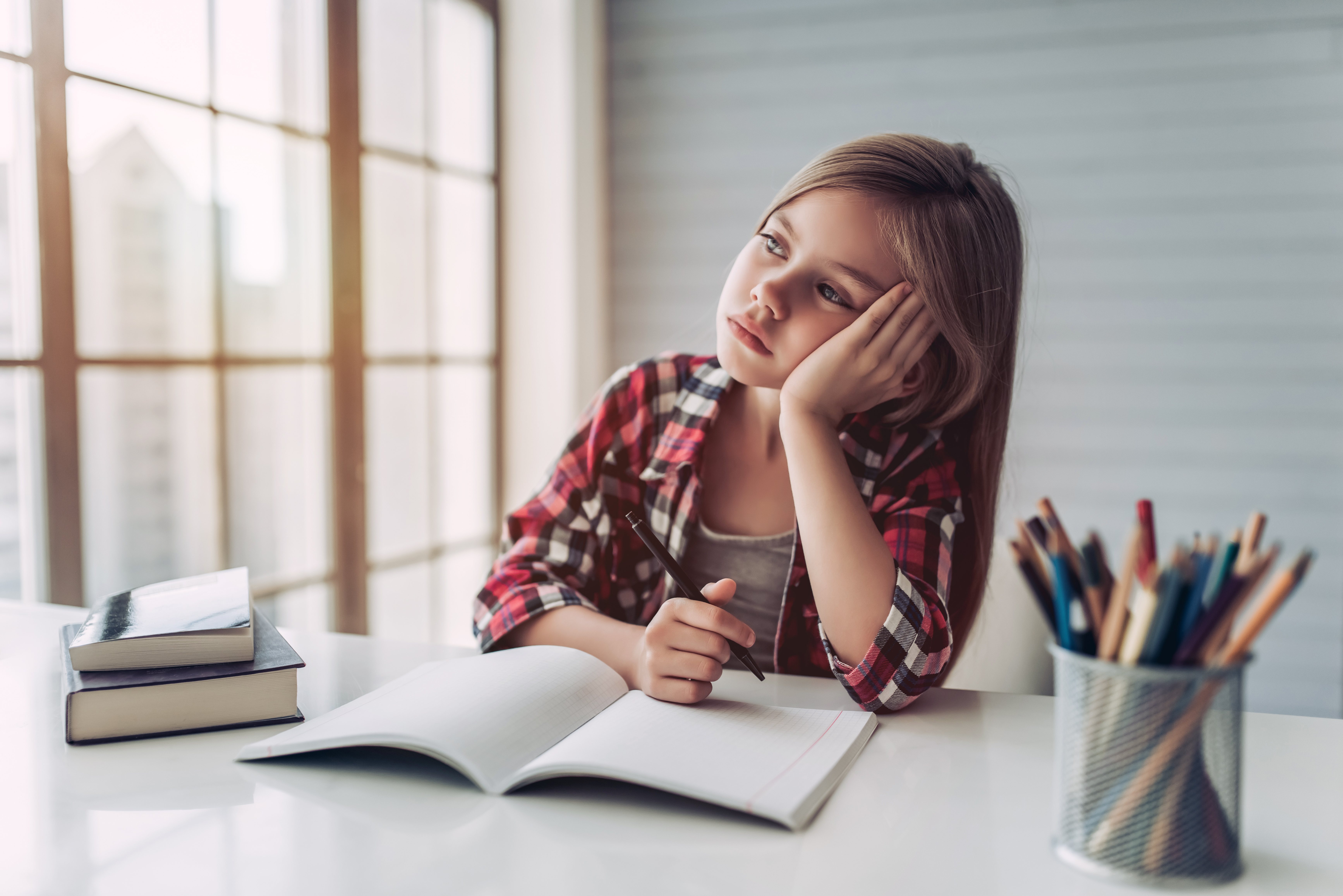 Chica joven mirando por la ventana desde su escritorio | Foto: Shutterstock