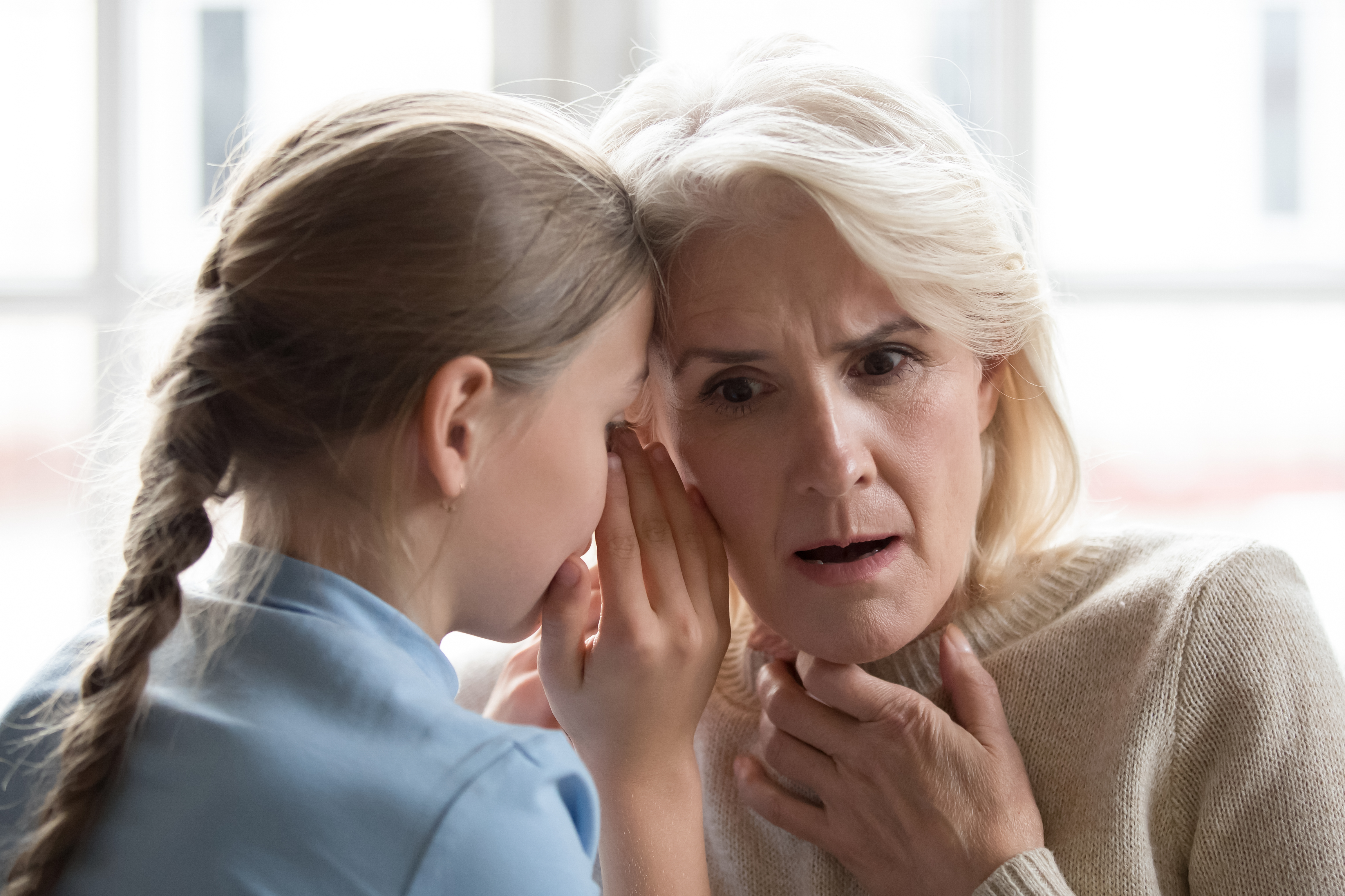 Niña susurrando algo a una mujer mayor | Foto: Shutterstock