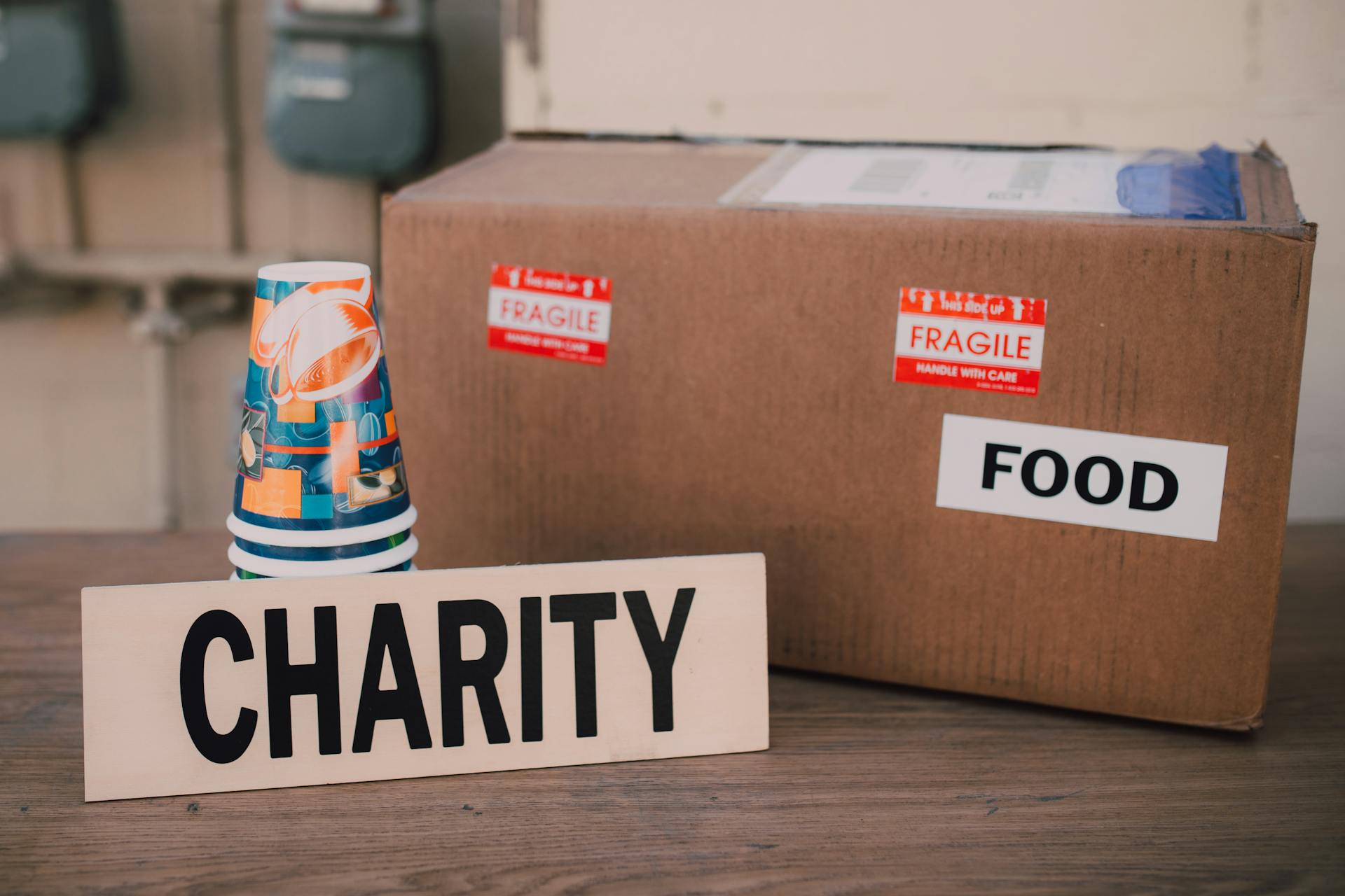 Una caja de cartón y una pila de vasos de papel junto a un cartel benéfico | Fuente: Pexels