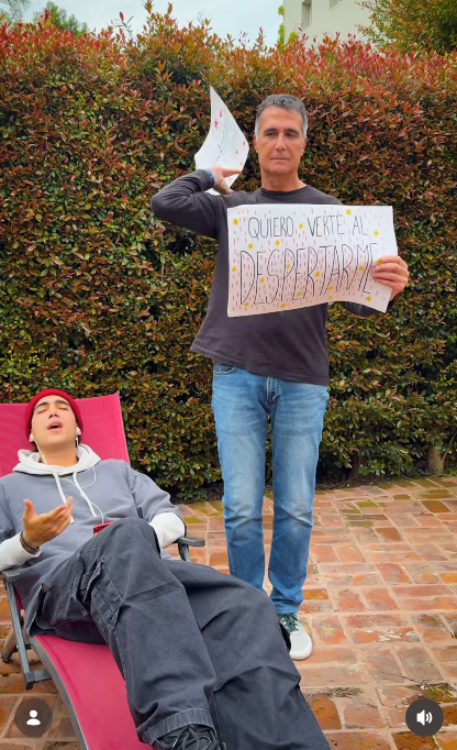 En plena sincronización con la letra, Antonio Laje lanzó una de las hojas por encima de su hombro mientras revelaba el nuevo cartel: "QUIERO VERTE AL DESPERTARME". A sus pies, su hijo Ezequiel interpretaba su flamante tema con auriculares conectados al teléfono móvil. | Fuente: Instagram/leish.ar