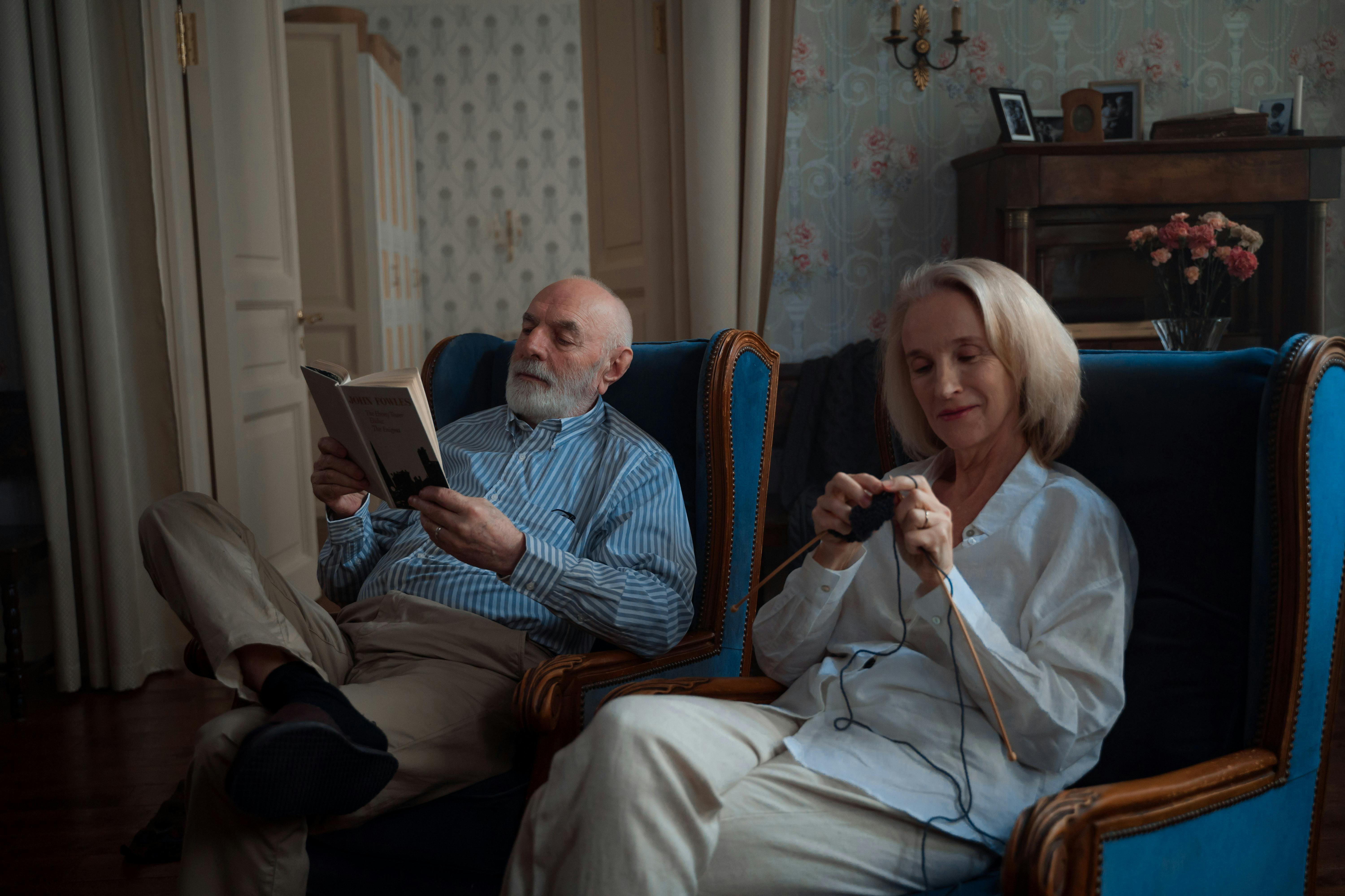 Un hombre lee mientras su esposa teje feliz | Fuente: Pexels