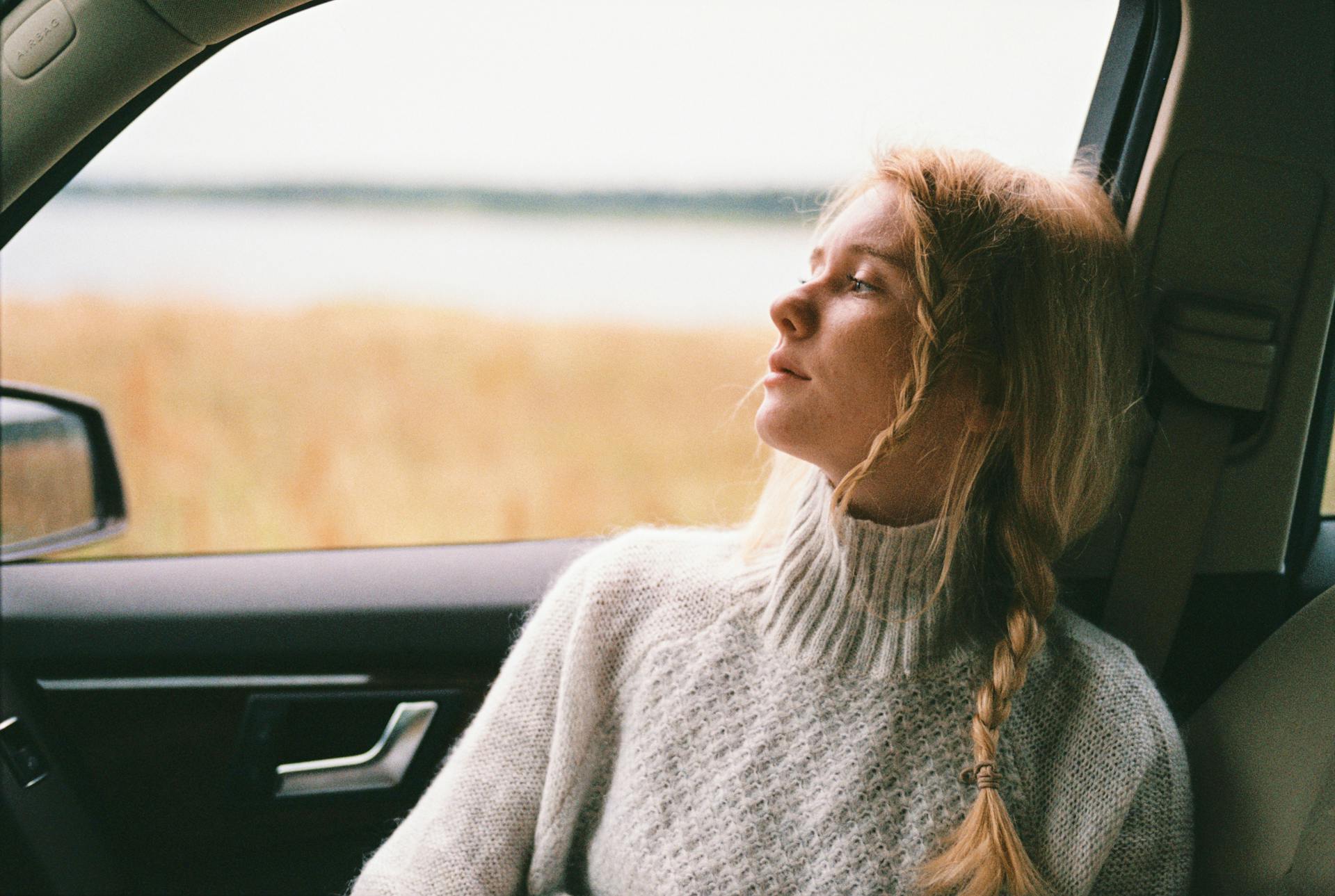 Una mujer con jersey sentada dentro de un Automóvil y pensando | Fuente: Pexels