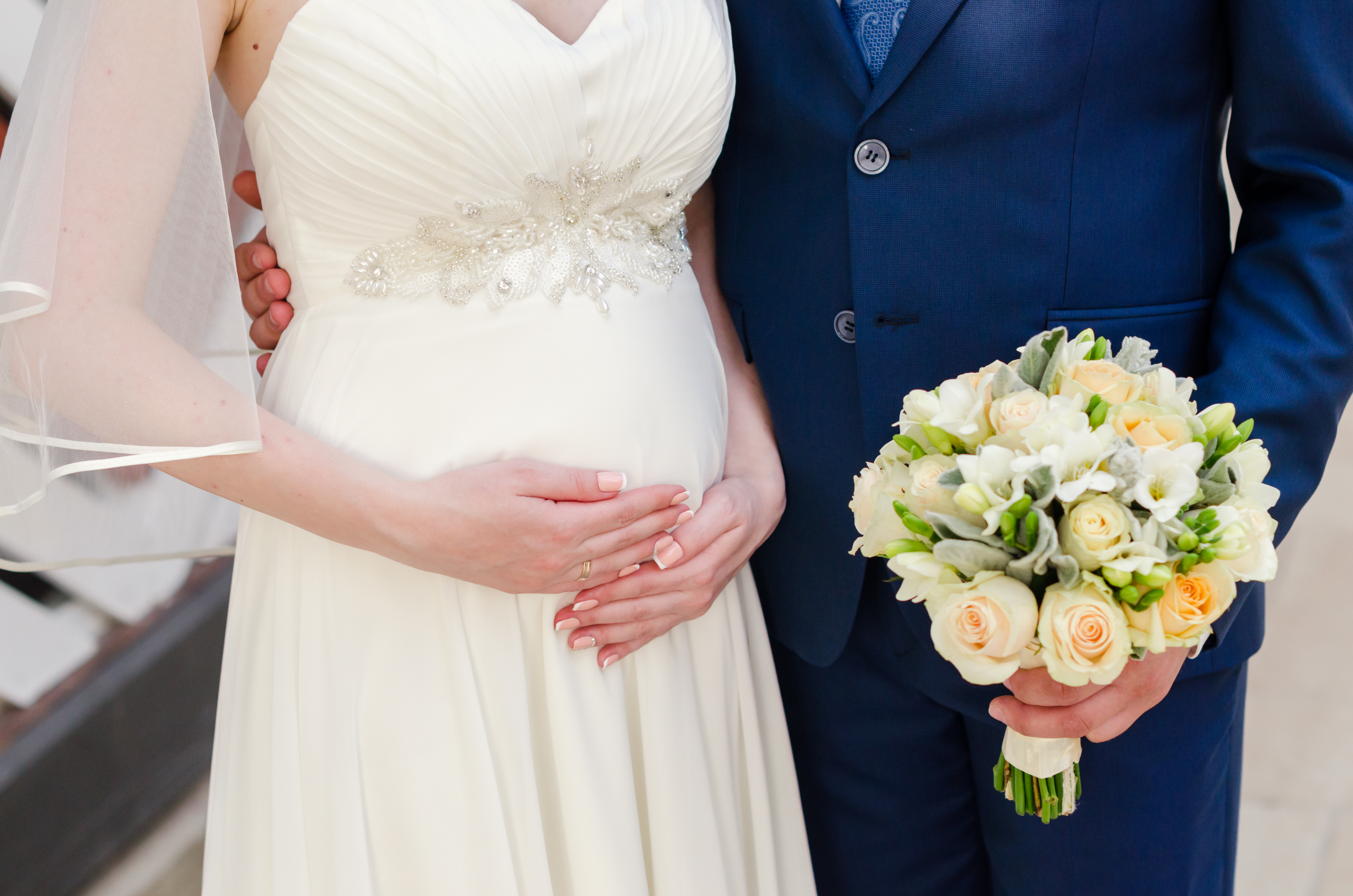 Una novia embarazada se sujeta el vientre mientras su novio le sostiene el ramo. | Foto: Shutterstock
