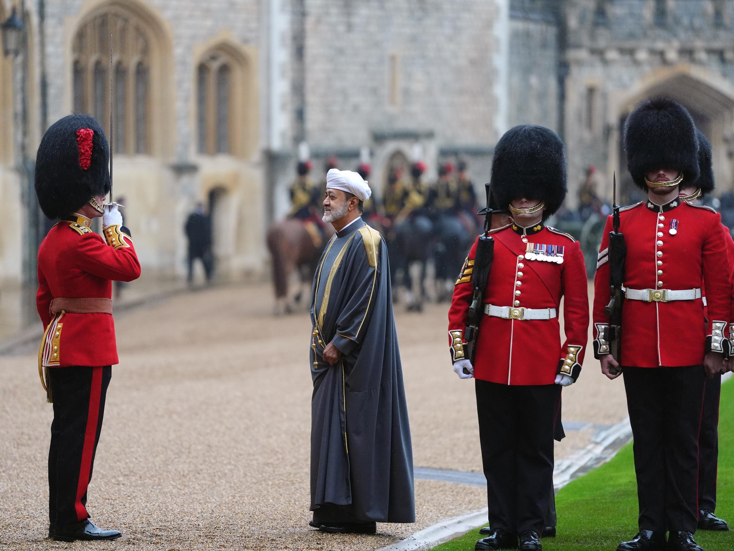 El sultán Haitham bin Tarik de Omán pasa revista a la Guardia de Honor durante la bienvenida ceremonial en el patio del castillo de Windsor, Inglaterra, el 20 de octubre de 2026. Viste un bisht gris hasta los tobillos con bordados dorados en hombros y bordes, y un turbante blanco. El monarca observa atento mientras un oficial con túnica roja y gorro de piel saluda con la espada en alto, junto a guardias con uniforme de gala. | Fuente: Getty Images
