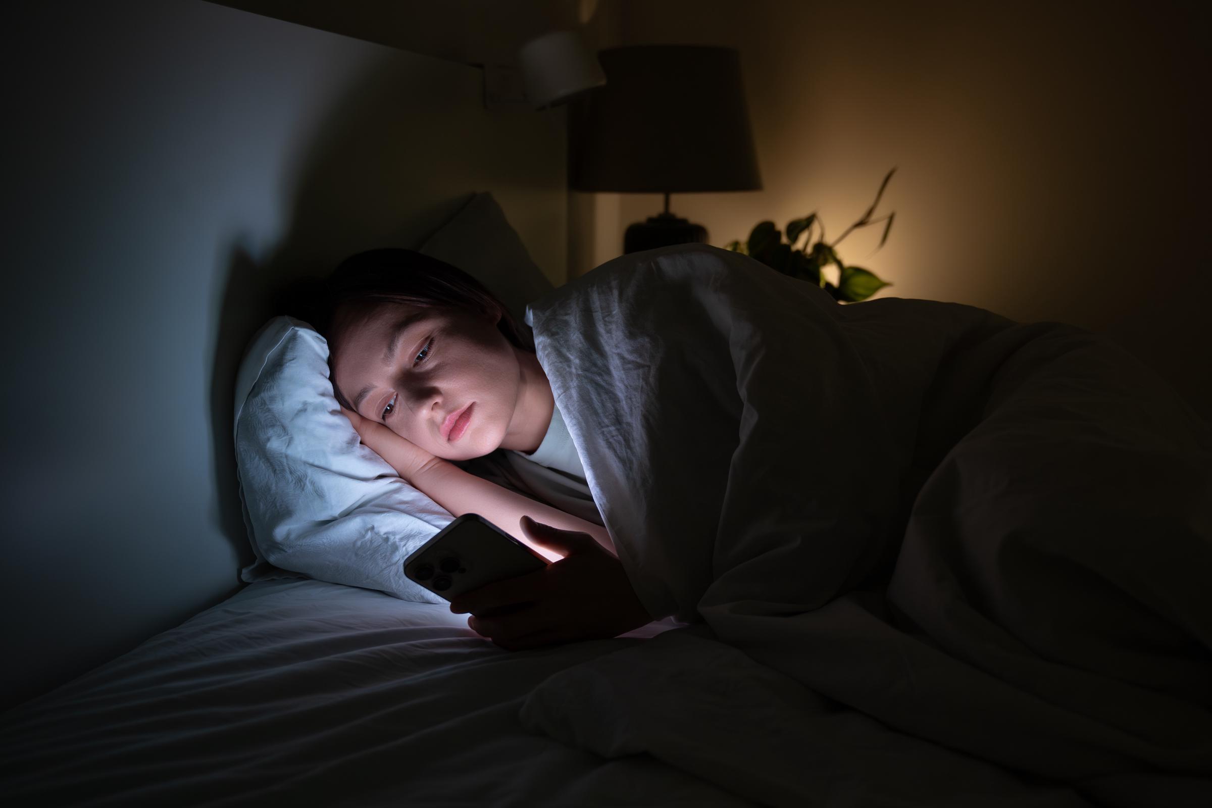 Una mujer haciendo scroll en su teléfono mientras está en la cama | Fuente: Getty Images
