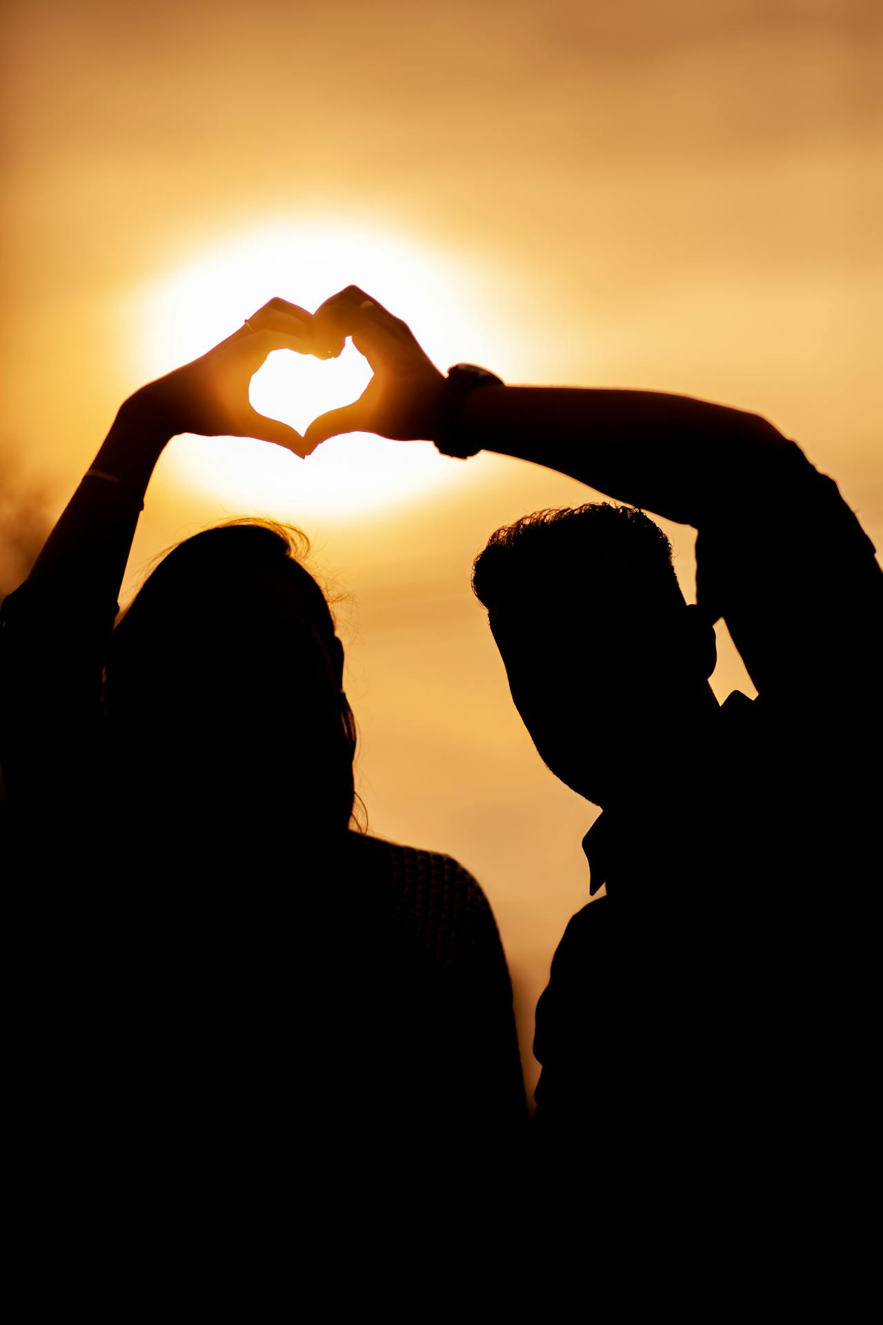 Silueta de una pareja haciendo un gesto de corazón con la mano | Fuente: Pexels