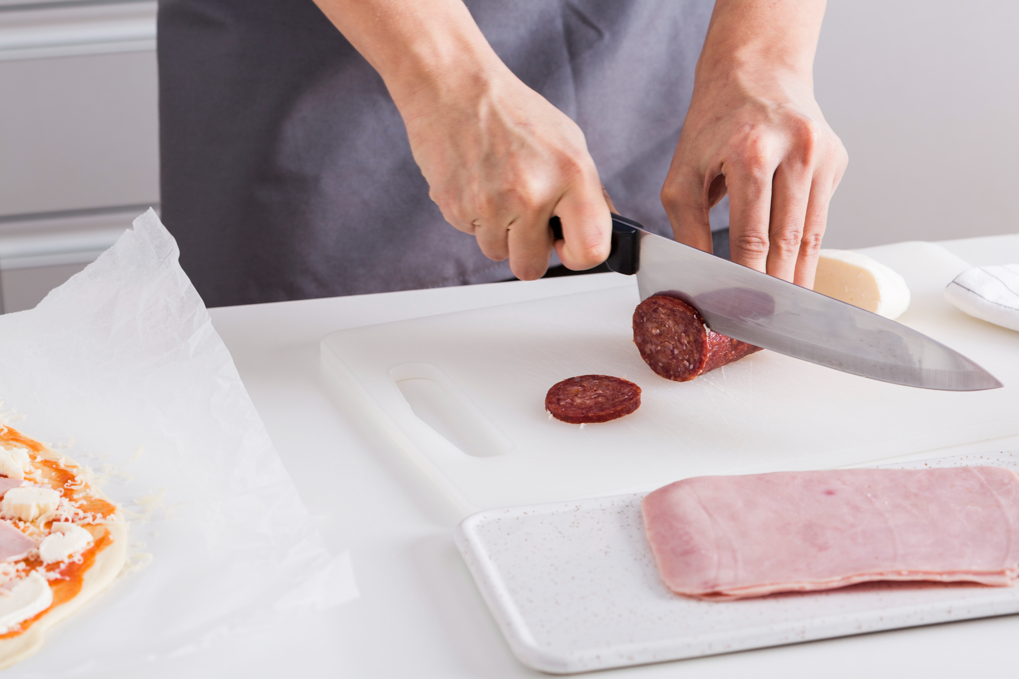 Una mujer cortando rodajas de salami en una tabla de cortar | Fuente: Freepik