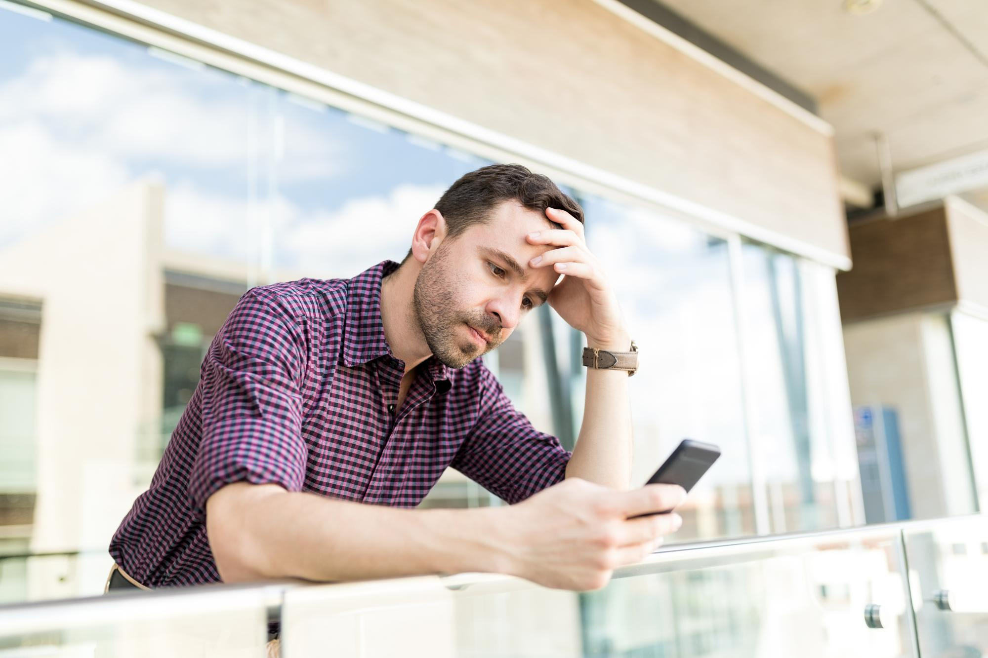 Hombre alterado en el balcón mirando su teléfono | Foto: Freepik