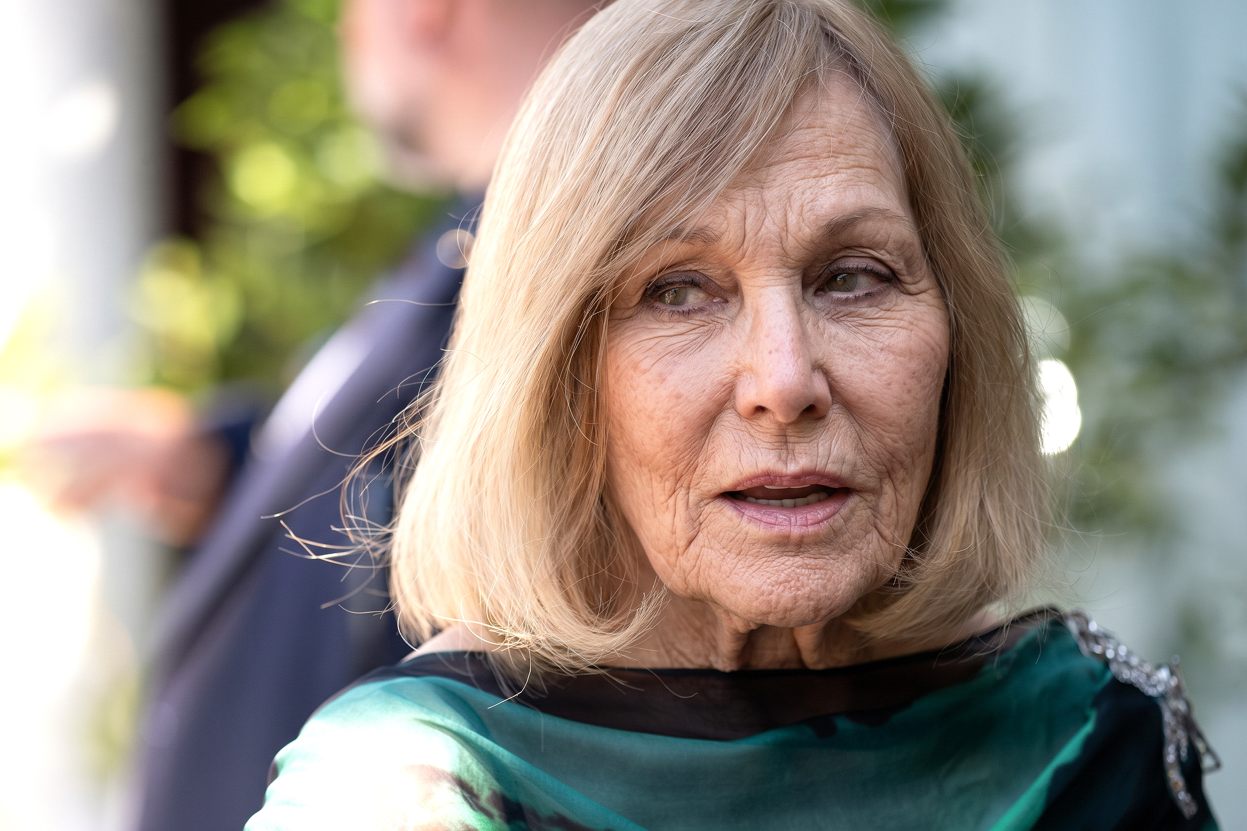 Kim Novak posa al aire libre con su conjunto verde y negro; su pelo rubio le enmarca la cara, mientras que la vegetación ligeramente difuminada a sus espaldas le da un toque natural. | Fuente: Gemini