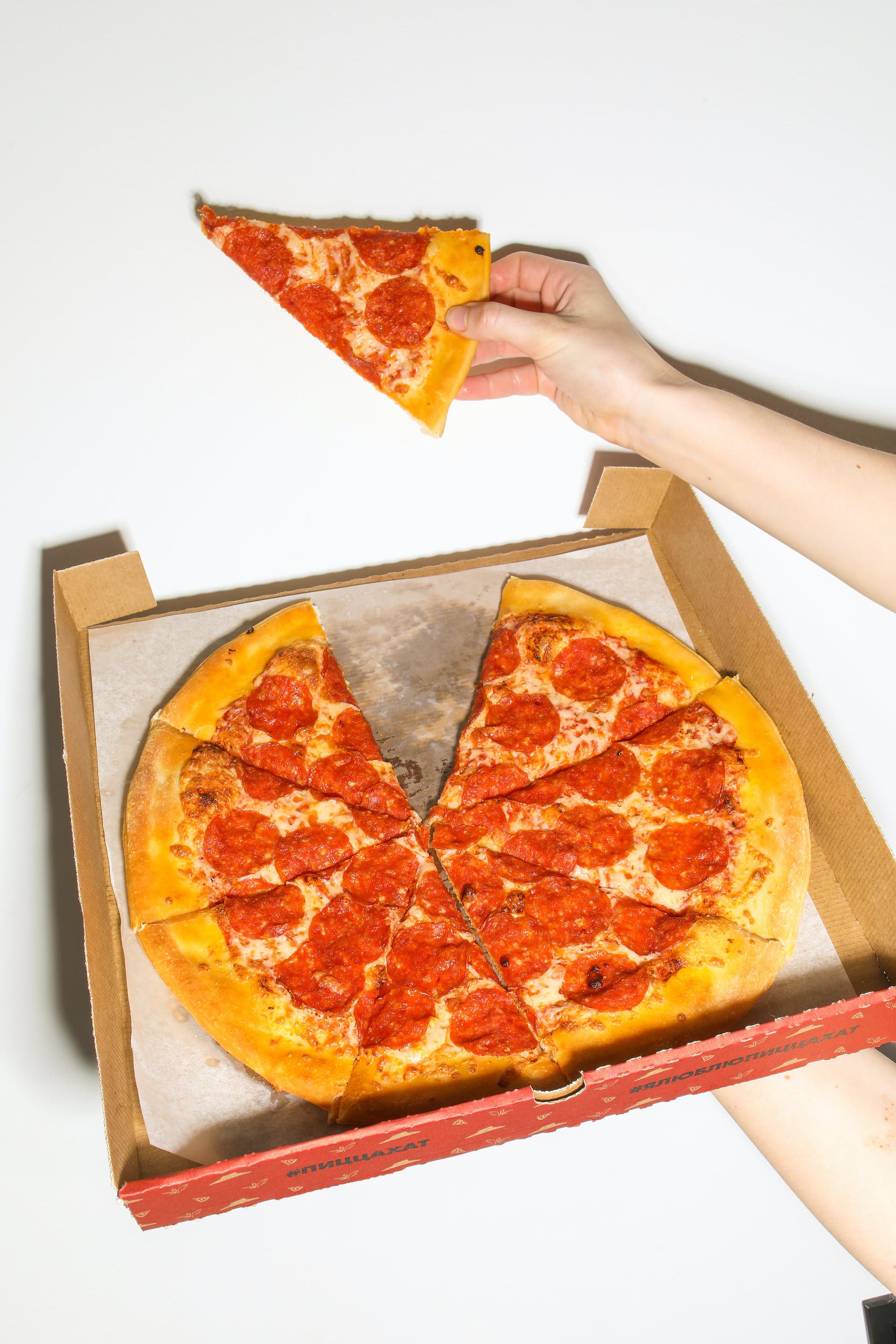 Una persona sujetando una porción de pizza y una caja de pizza | Fuente: Pexels