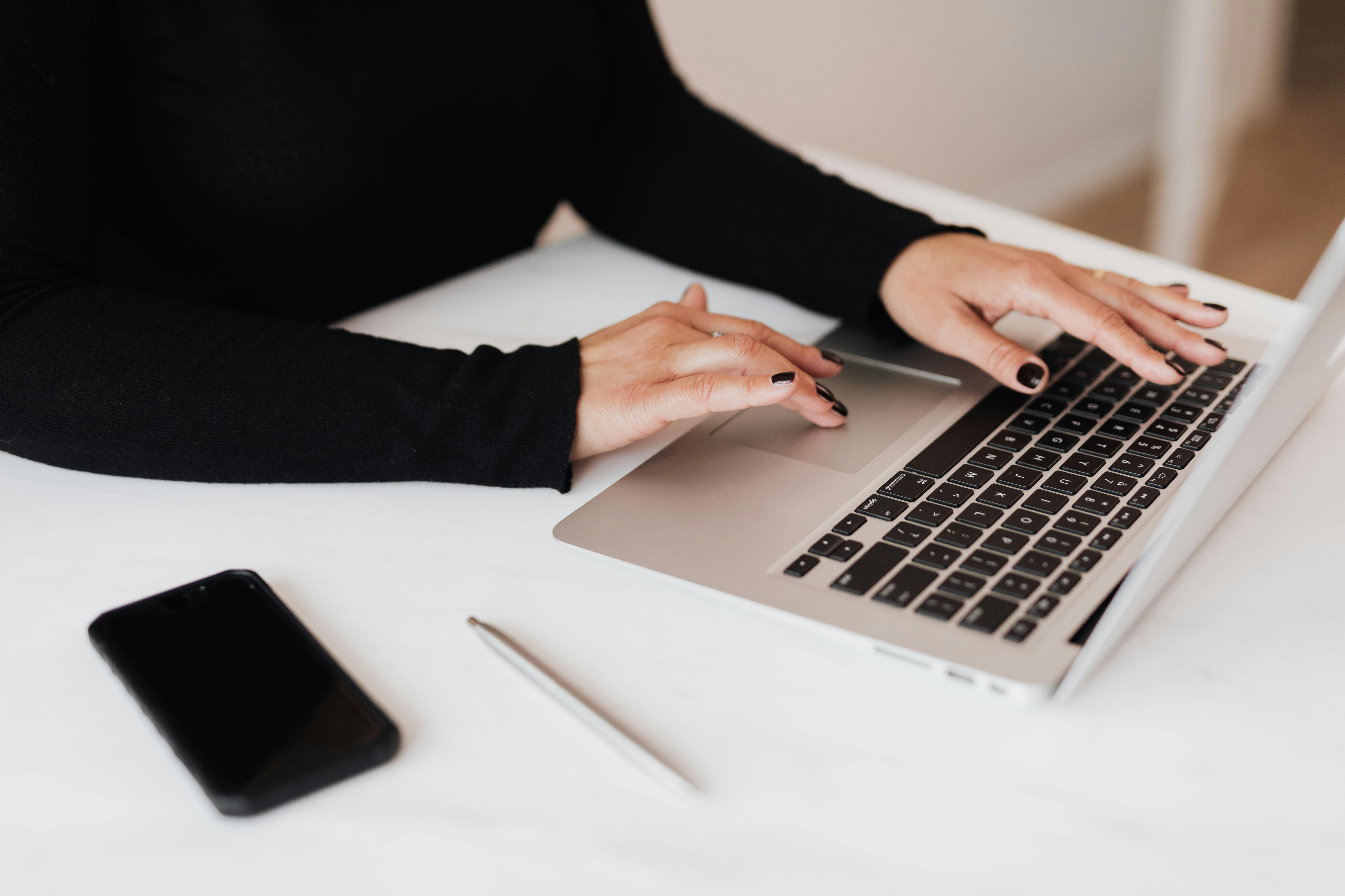 Una mujer usando su portátil con su teléfono cerca | Fuente: Pexels