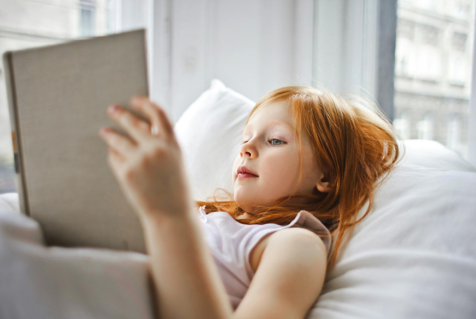 Una niña con un libro en la cama | Fuente: Pexels