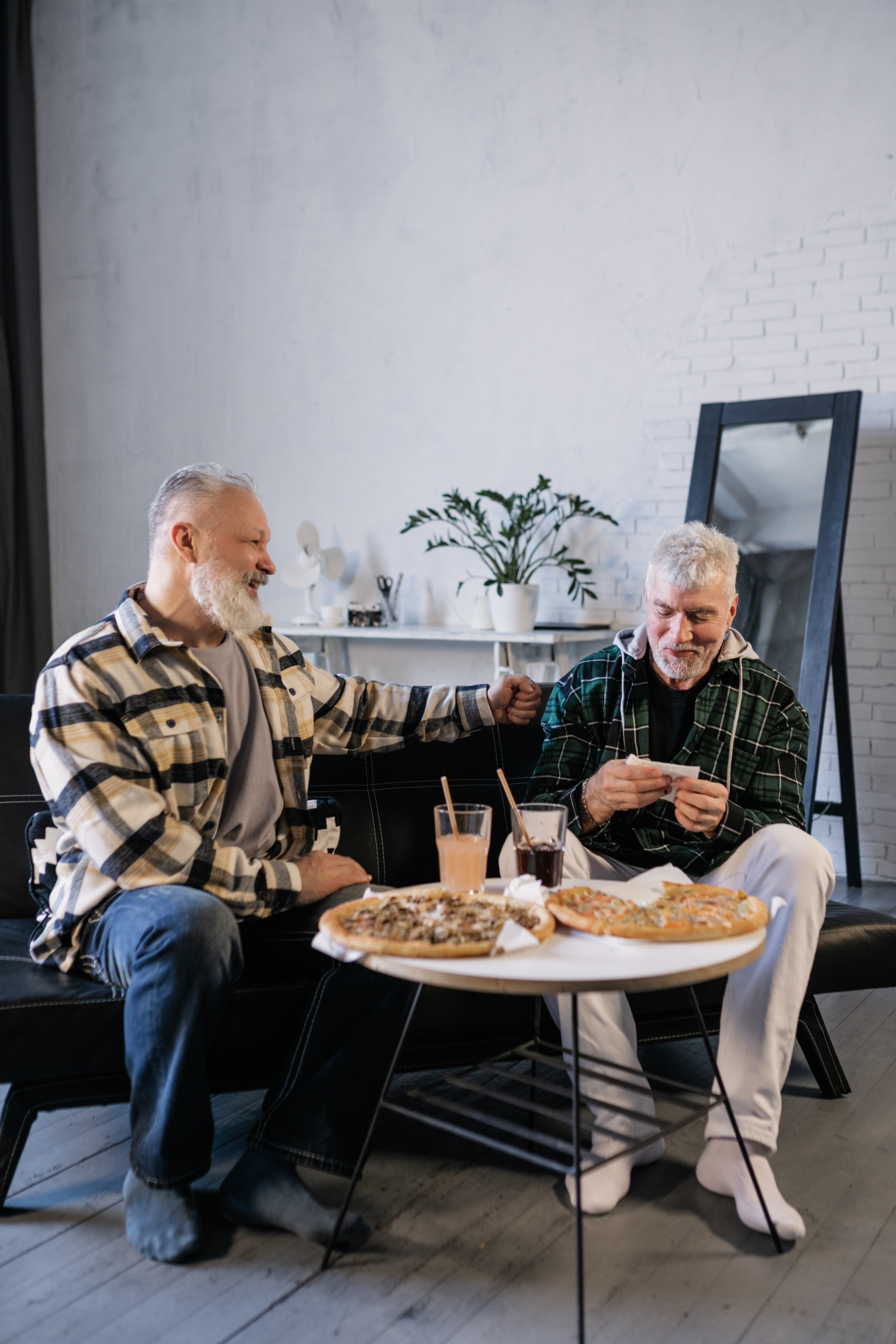 Dos hombres mayores sentados en un sofá mientras comen y conversan. | Foto: Pexels
