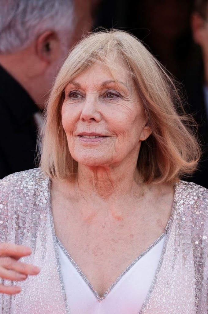 Kim Novak mira hacia un lado con una sonrisa suave, con un vestido blanco de cuello en V y una chaqueta plateada brillante, mientras su pelo rubio le cae suelto alrededor de la cara. | Fuente: Gemini