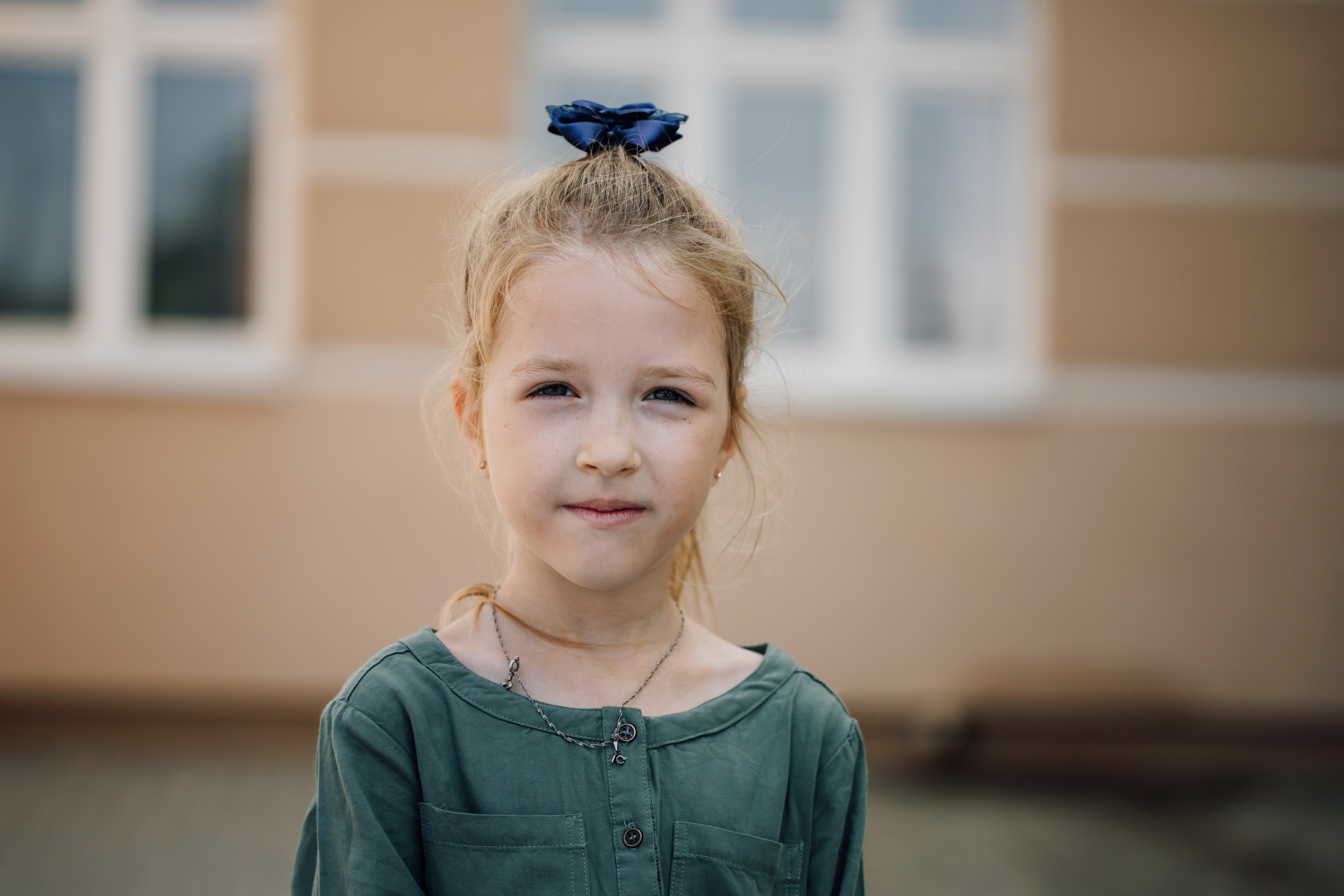 Retrato de niña seria mirando a cámara con edificio de escuela primaria de fondo | Foto: Getty Images