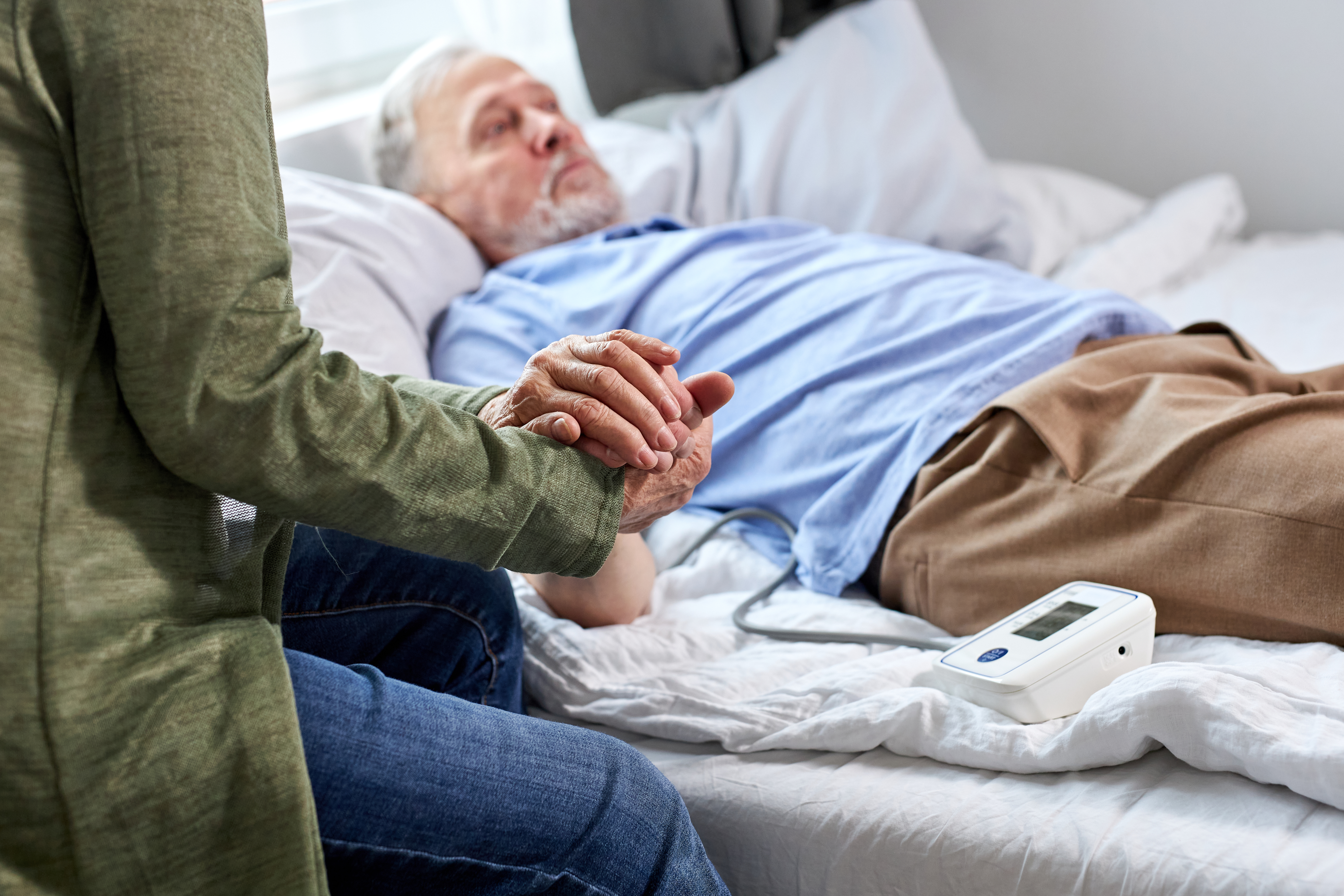 Una mujer coge de la mano a un anciano enfermo mientras está sentada a su lado | Fuente: Shutterstock
