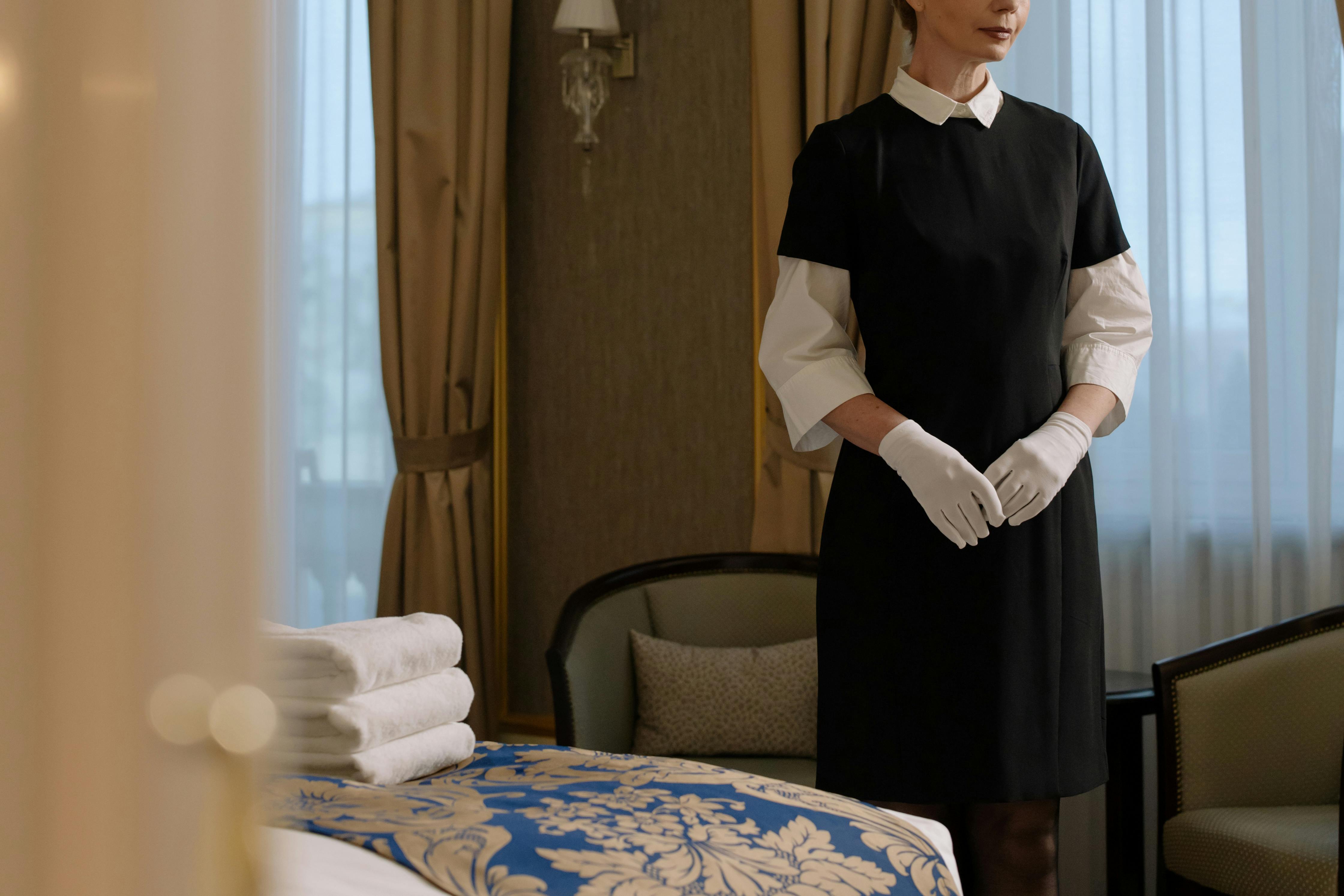 Mujer de uniforme junto a la cama de una habitación de hotel | Fuente: Pexels
