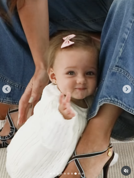 Asomándose entre las piernas de su mamá, la bebé saludó con su manito extendida hacia la cámara con un gesto dulce y travieso. En la toma se aprecian las sandalias de tiras cruzadas y hebilla dorada que lució Camila junto a sus jeans acampanados. | Fuente: Instagram/camihoms