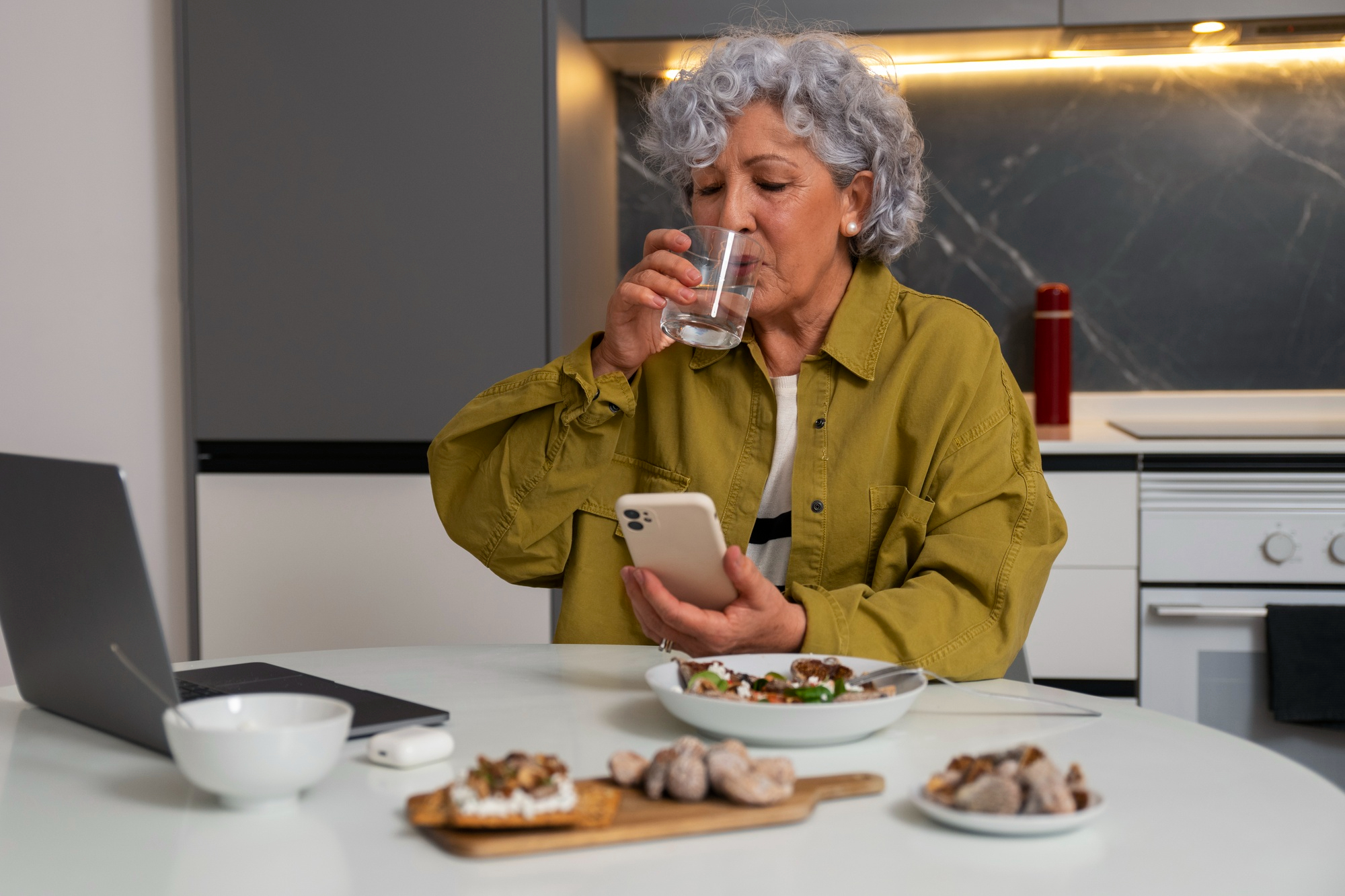 Una mujer sentada en la cocina disfrutando de una comida y mirando su teléfono. Imagen con fines ilustrativos | Foto: Freepik