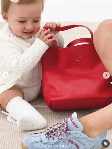 La pequeña Aitana protagonizó un simpático momento jugando en el piso con una cartera tote roja con manijas cortas de la firma, acompañada en primer plano por las zapatillas deportivas celestes de la colaboración y sus detalles bordados. | Fuente: Instagram/camihoms