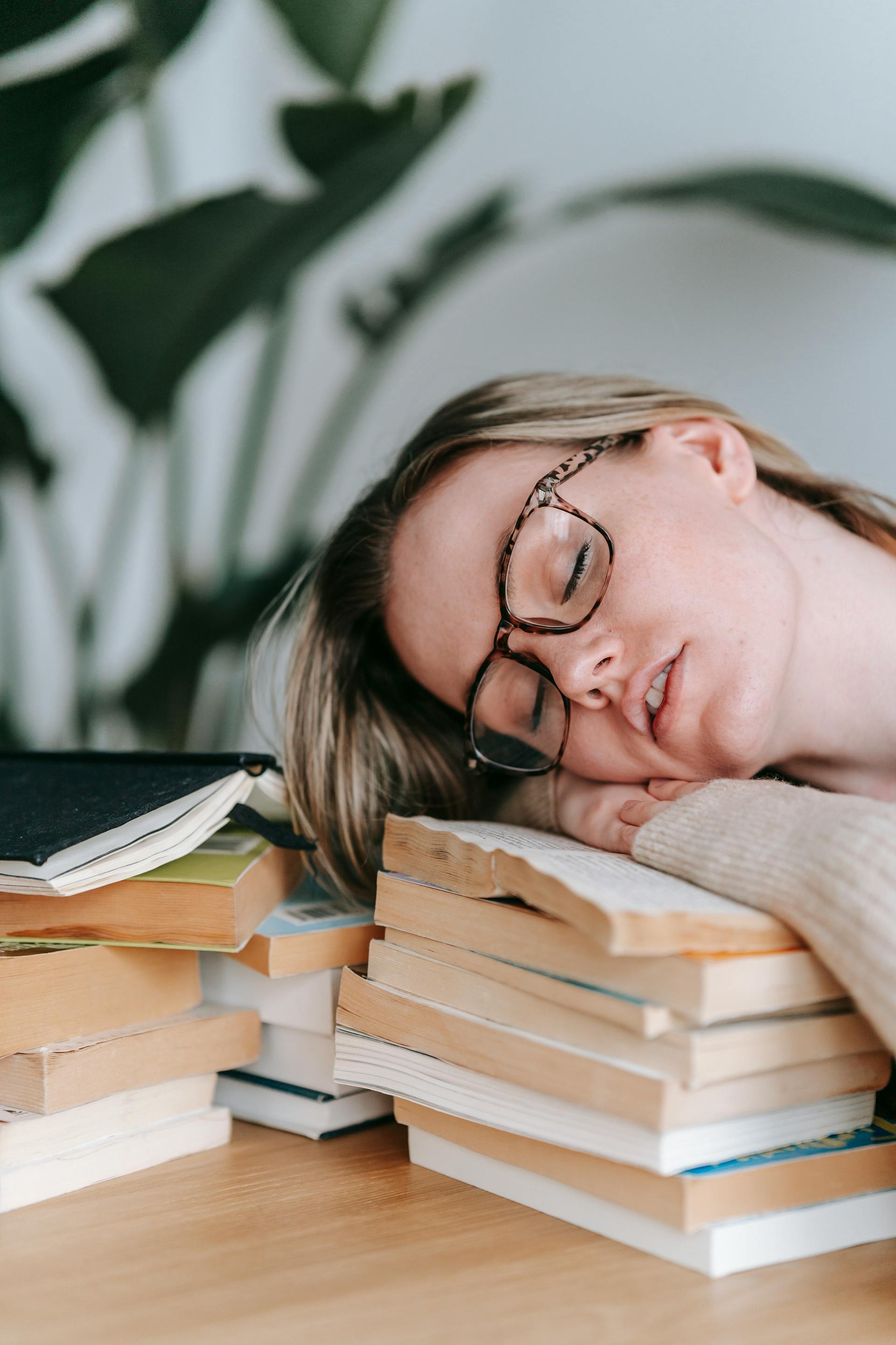 Una joven cansada descansa la cabeza sobre una pila de libros | Fuente: Pexels