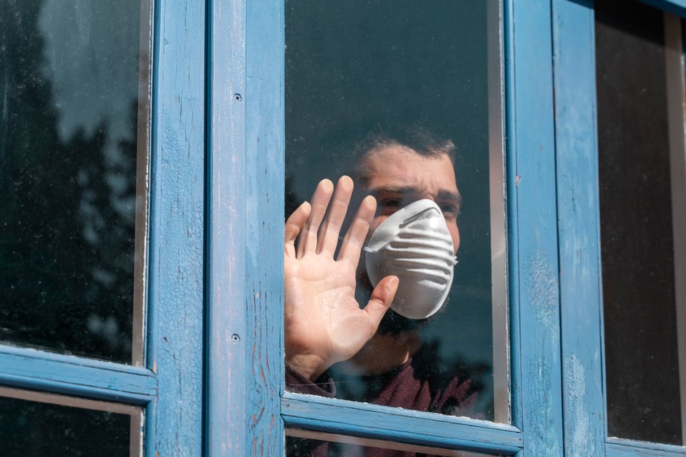 Un hombre con mascarilla asomado por una ventana. | Foto: Shutterstock