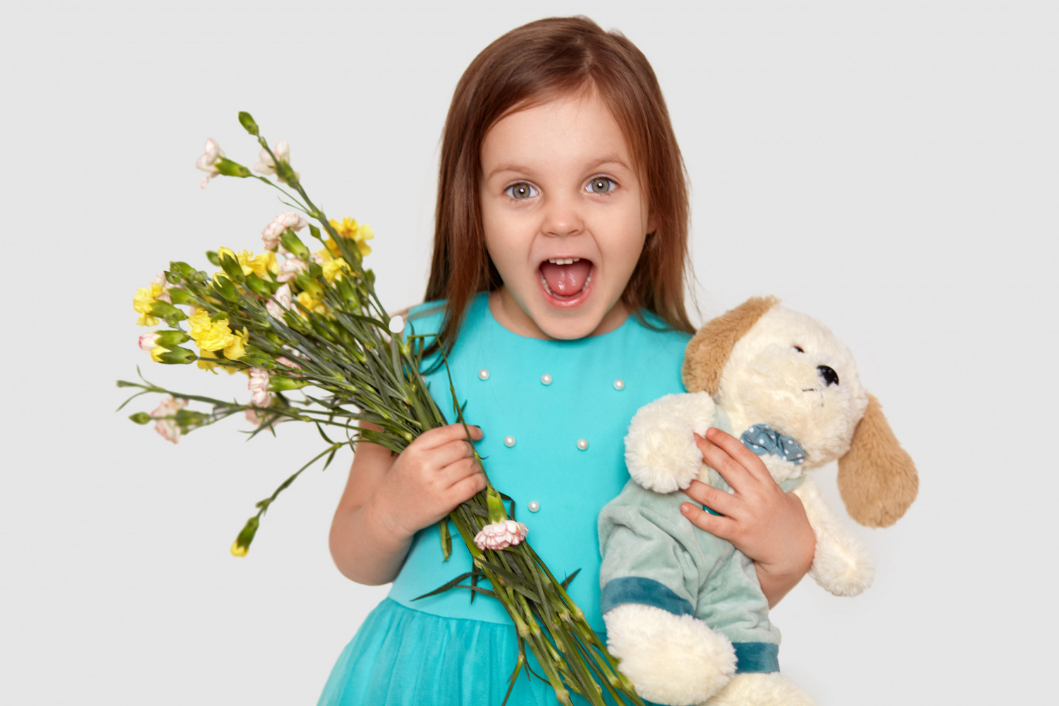 Una niña encantada sosteniendo flores y un peluche | Fuente: Freepik